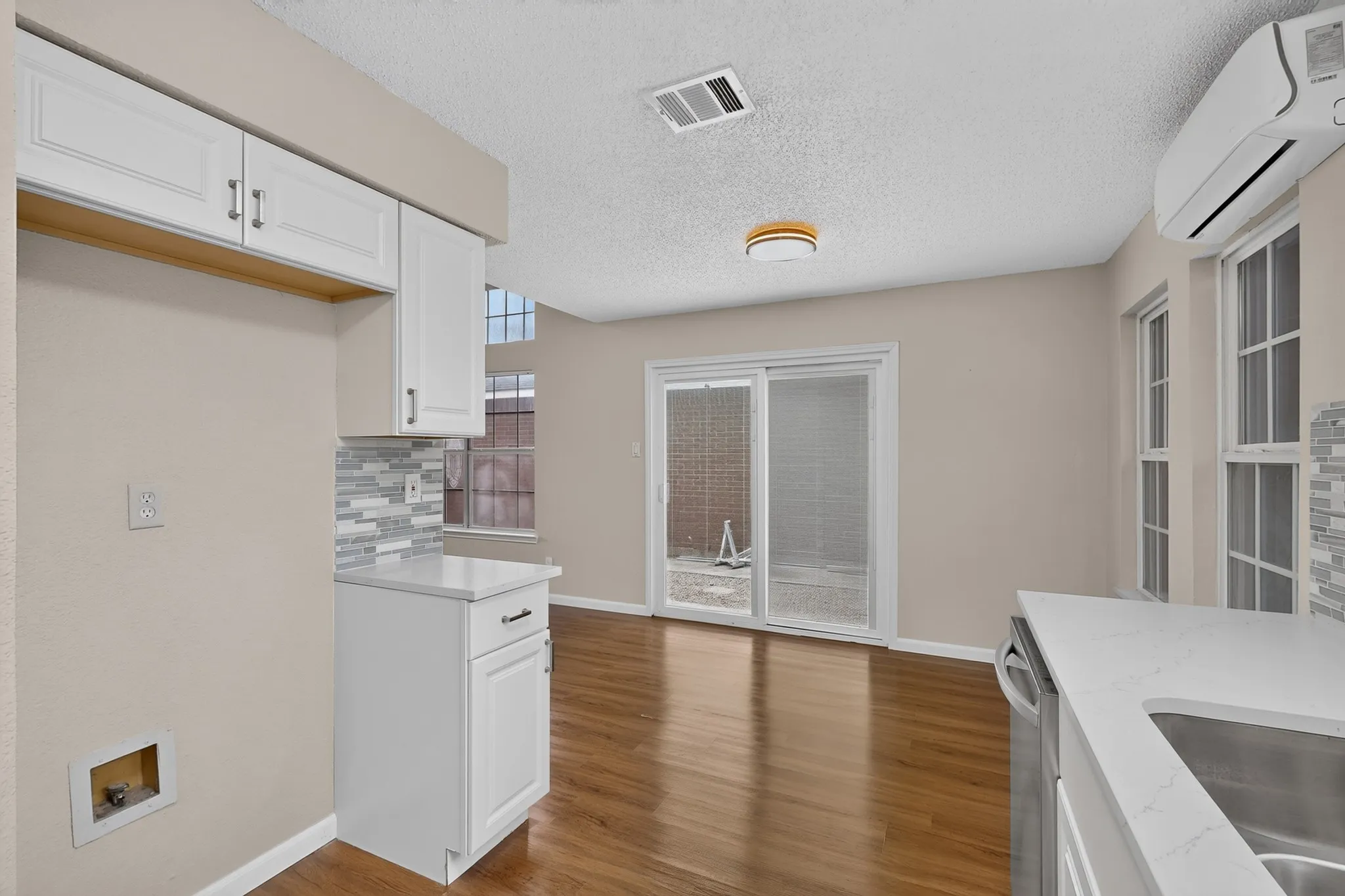 White cabinetry with dark hardware, stone-finish countertops, wood-finish flooring, sliding glass door, and multiple windows