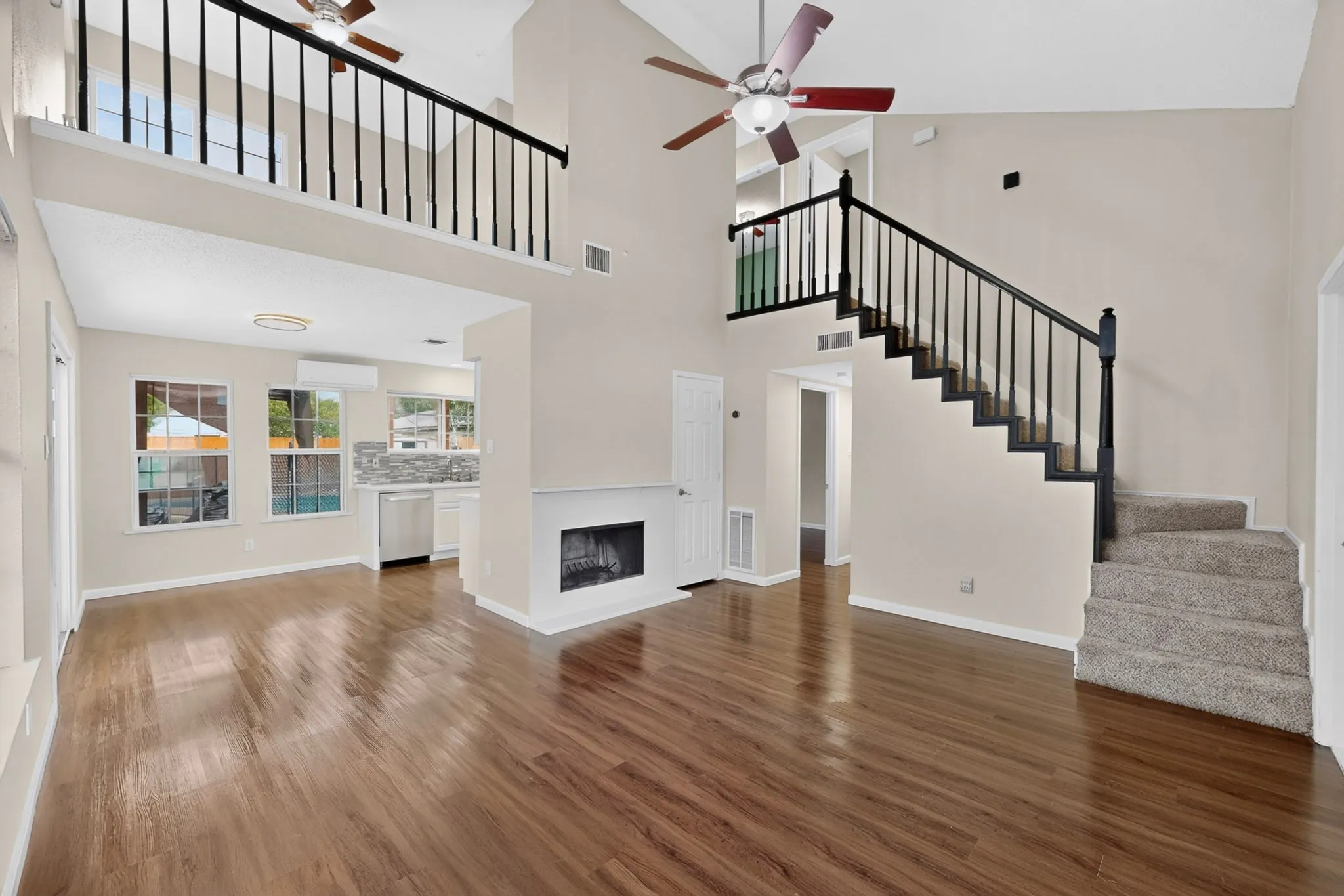 Open-concept living space featuring wood-finish flooring, a fireplace, and a carpeted staircase with a dark wood banister