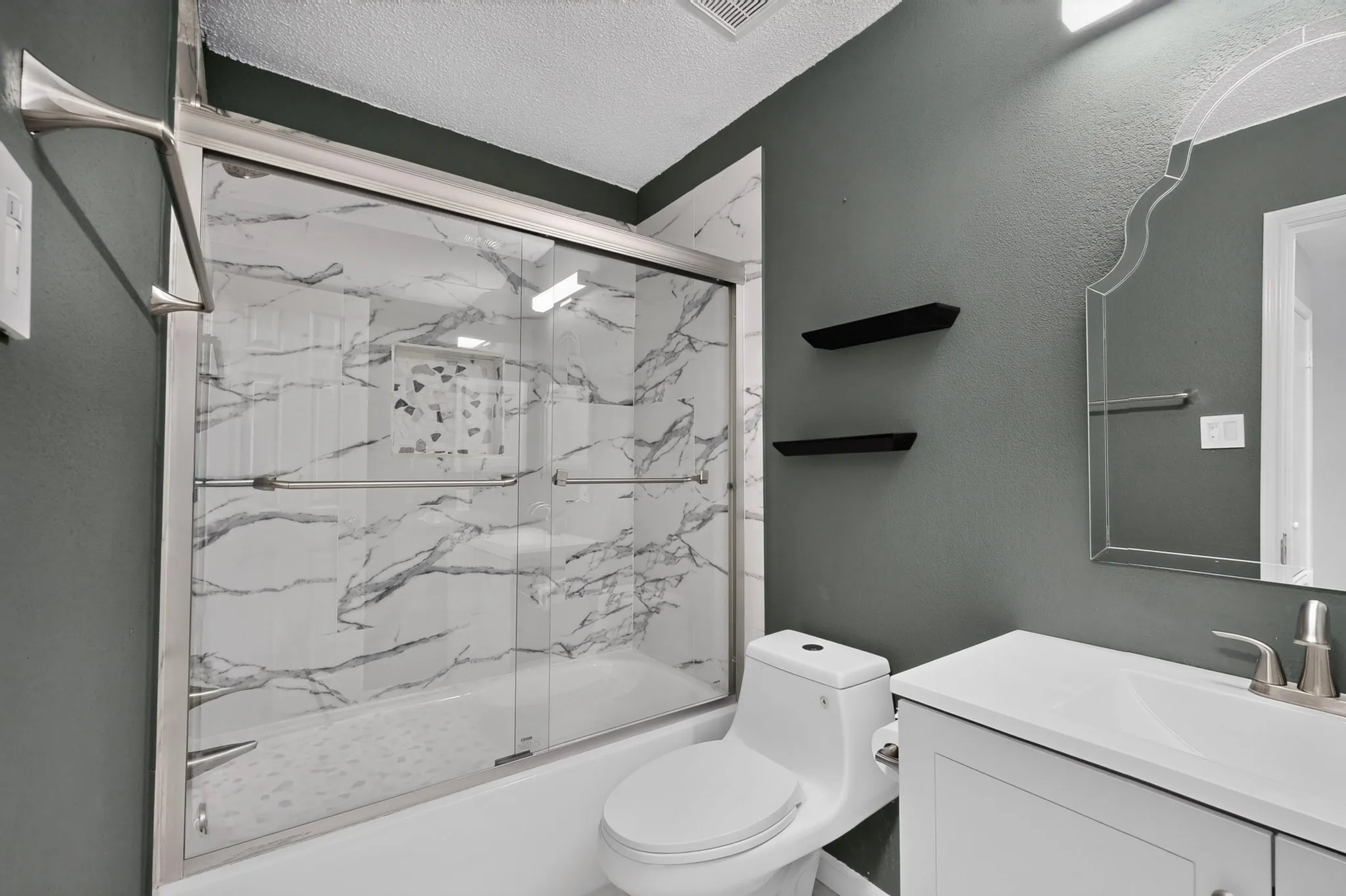 Tub with sliding glass enclosure, white marble-look surround, white vanity with integrated sink, and decorative mirror