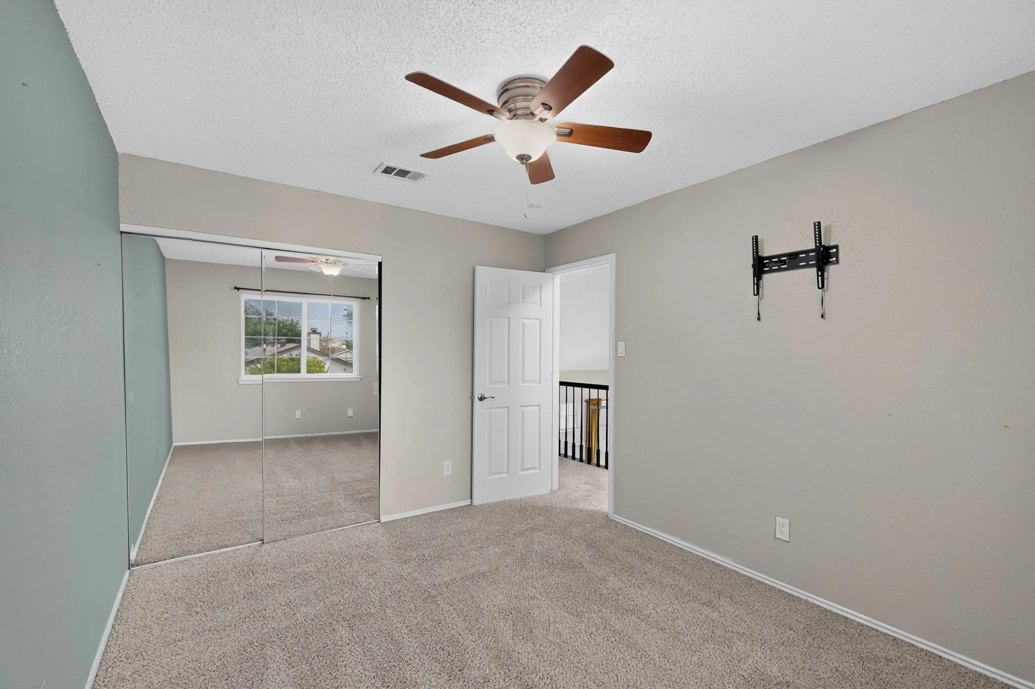 Carpeted flooring, mirrored sliding closet doors, ceiling fan with integrated lighting, wall-mounted television bracket