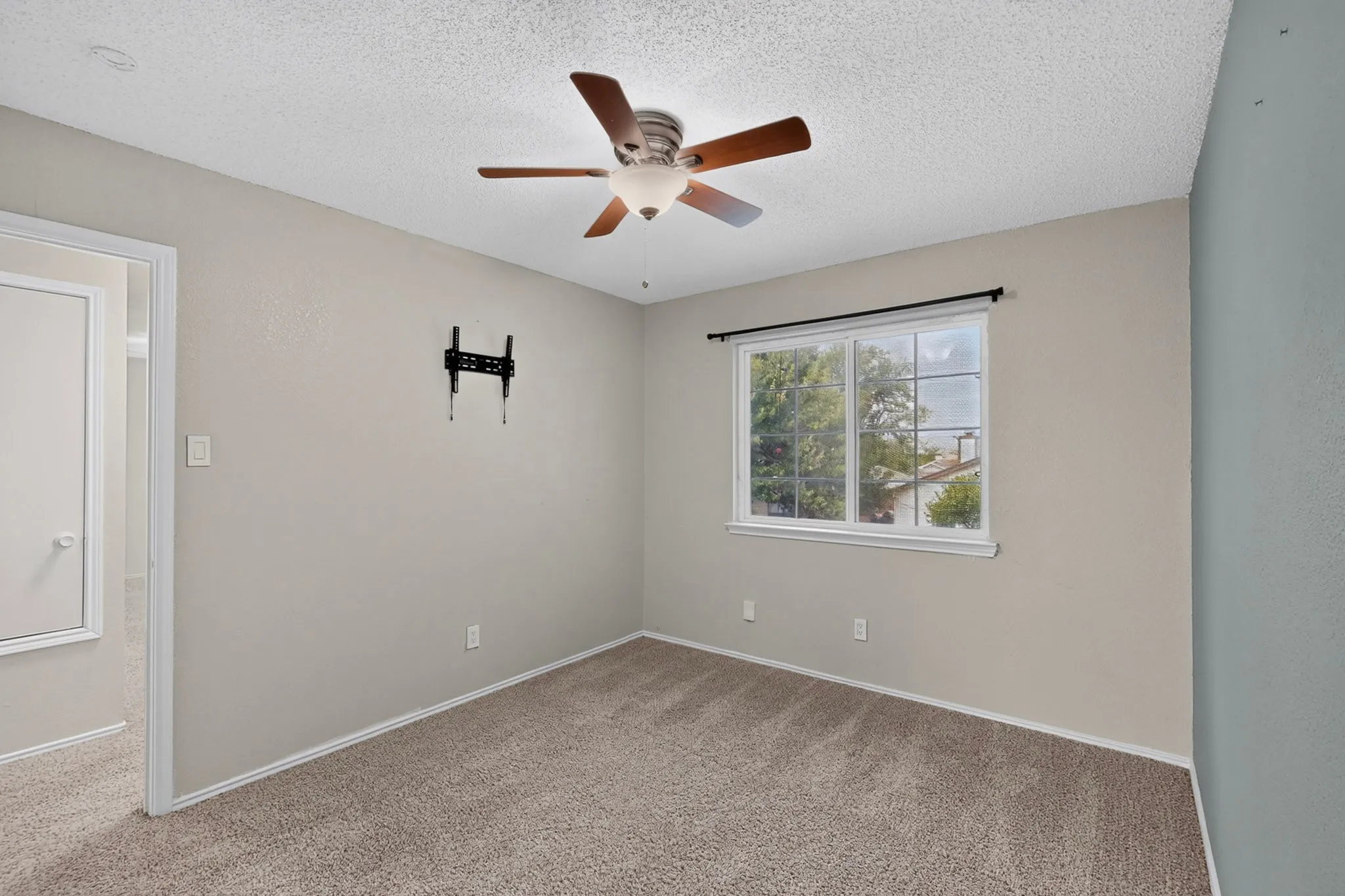 Textured carpet flooring, window with exterior landscape, ceiling fan with light fixture, neutral wall paint, and white trim