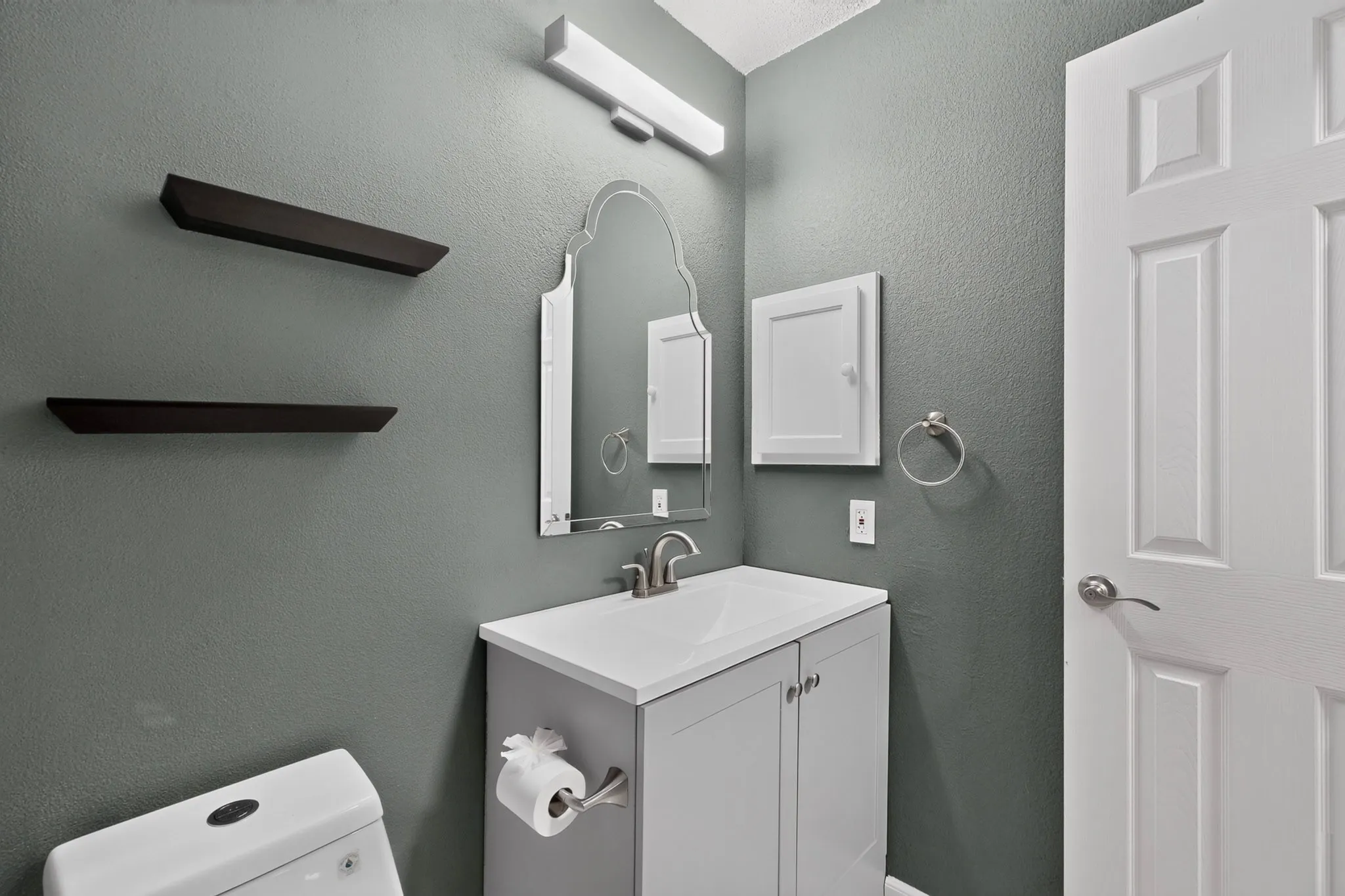 White vanity with an integrated sink and brushed nickel faucet, wall-mounted mirror, recessed medicine cabinet, and panel door