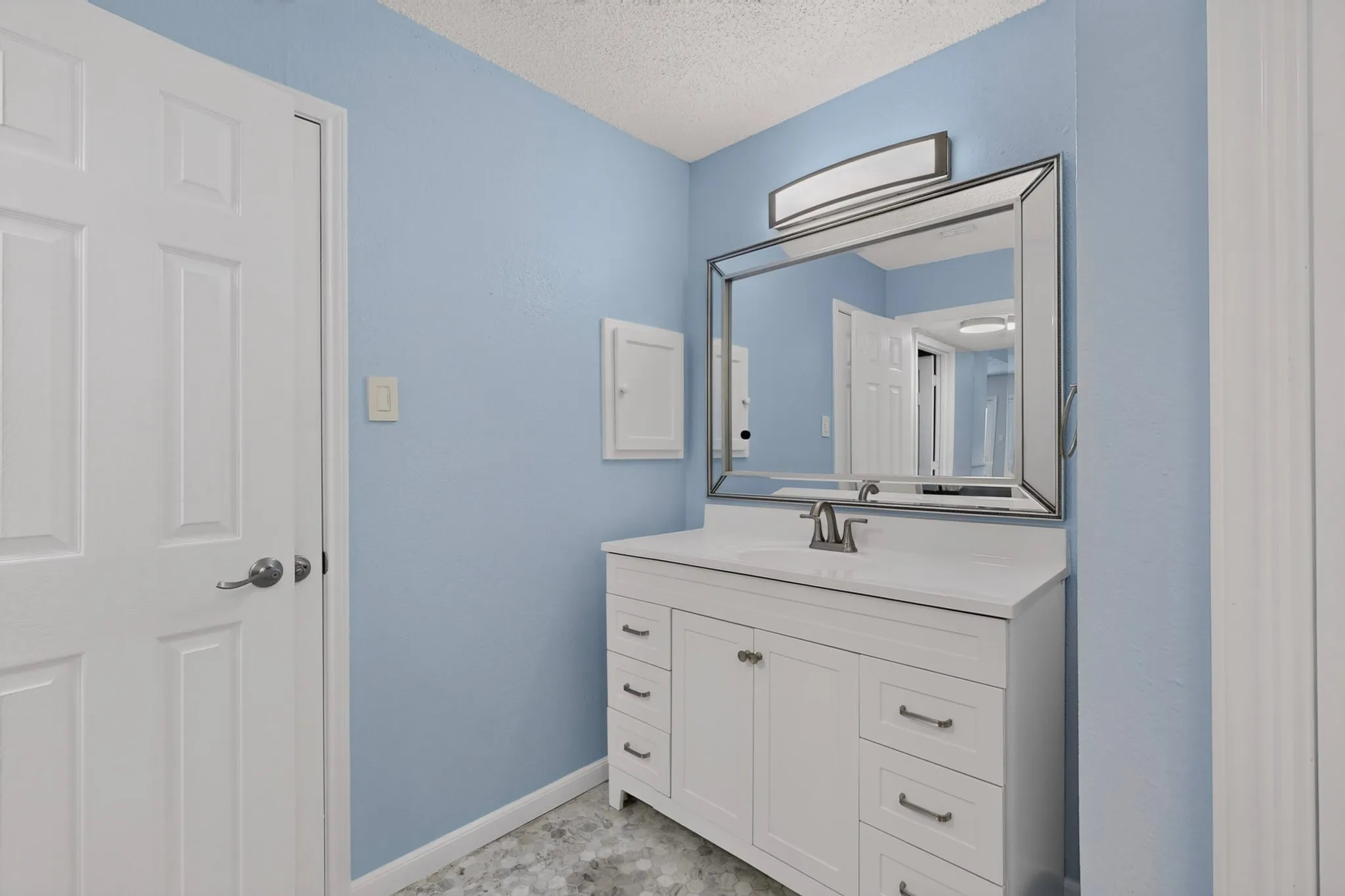 White vanity cabinet with integrated sink, rectangular framed mirror, and chrome-finish fixtures
