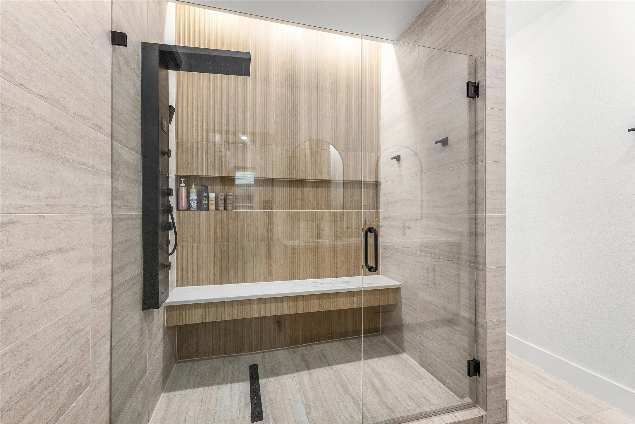 Glass-enclosed shower with a built-in bench, integrated shelving, and a matte black shower panel system