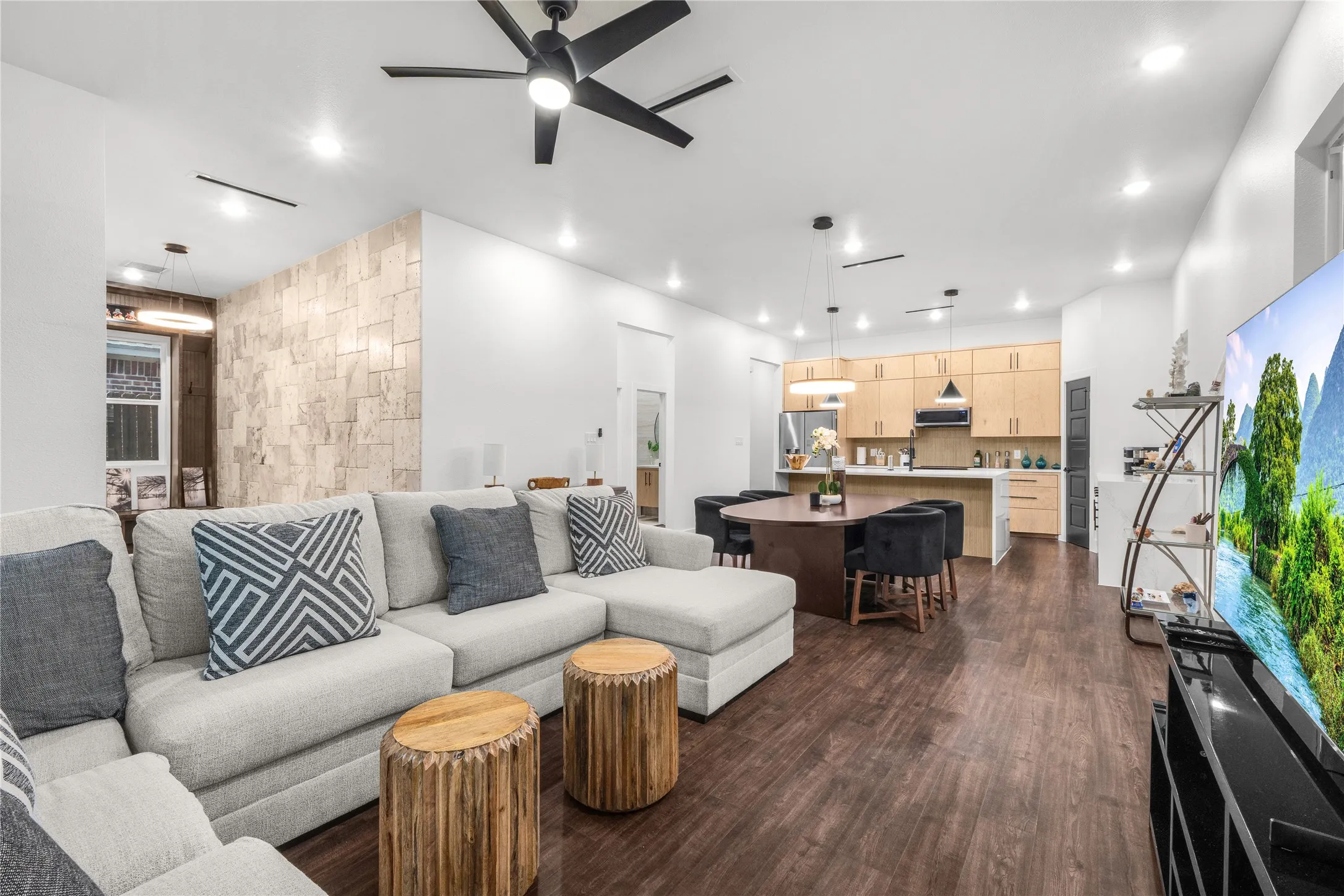 Open-concept living area with dark wood-finish flooring, a stone-accent wall, and recessed lighting