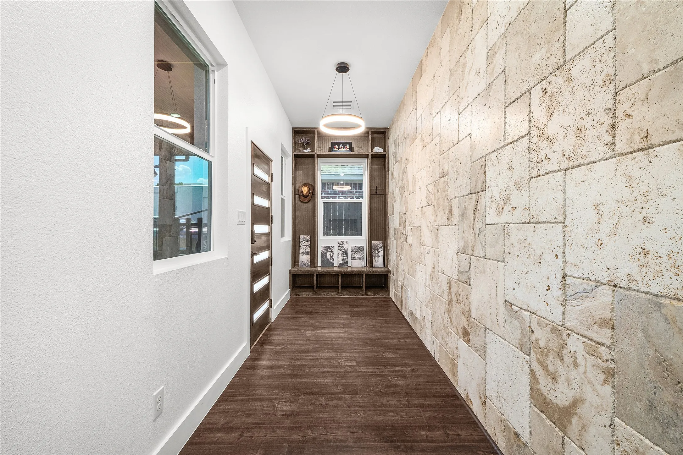 Hallway featuring a textured stone-finish accent wall, wood-finish flooring, a built-in bench with shelving, and a modern circular pendant light