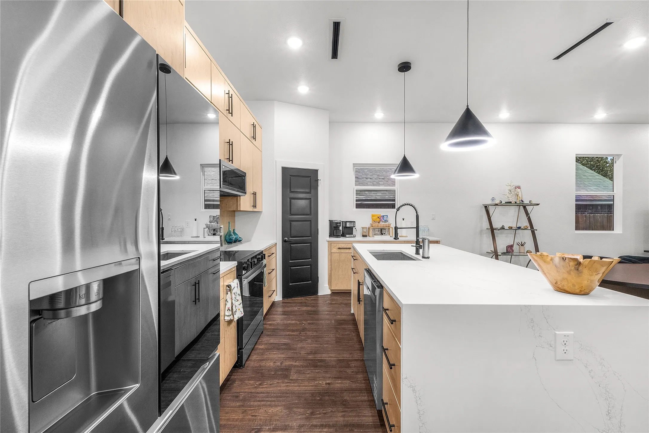 Stainless steel refrigerator, light wood-finish cabinetry, white countertops, built-in stainless steel appliances, and dark wood-finish flooring