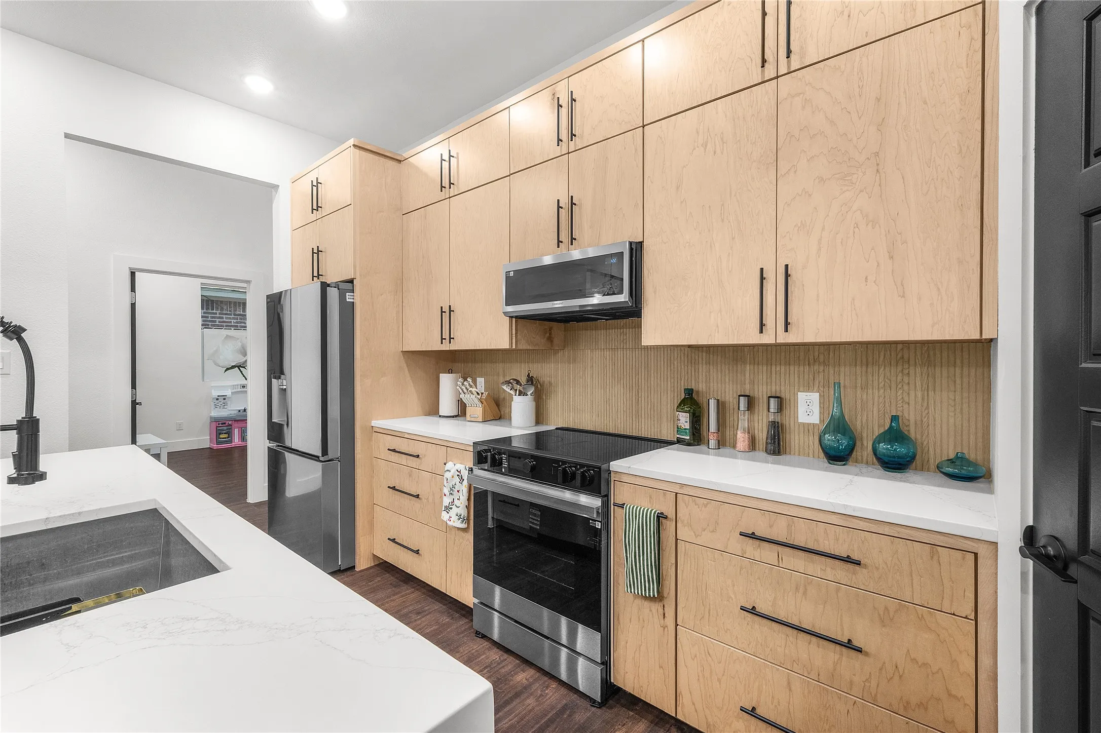 Sleek kitchen featuring light wood cabinetry, white countertops, a stainless steel refrigerator, and a built-in microwave