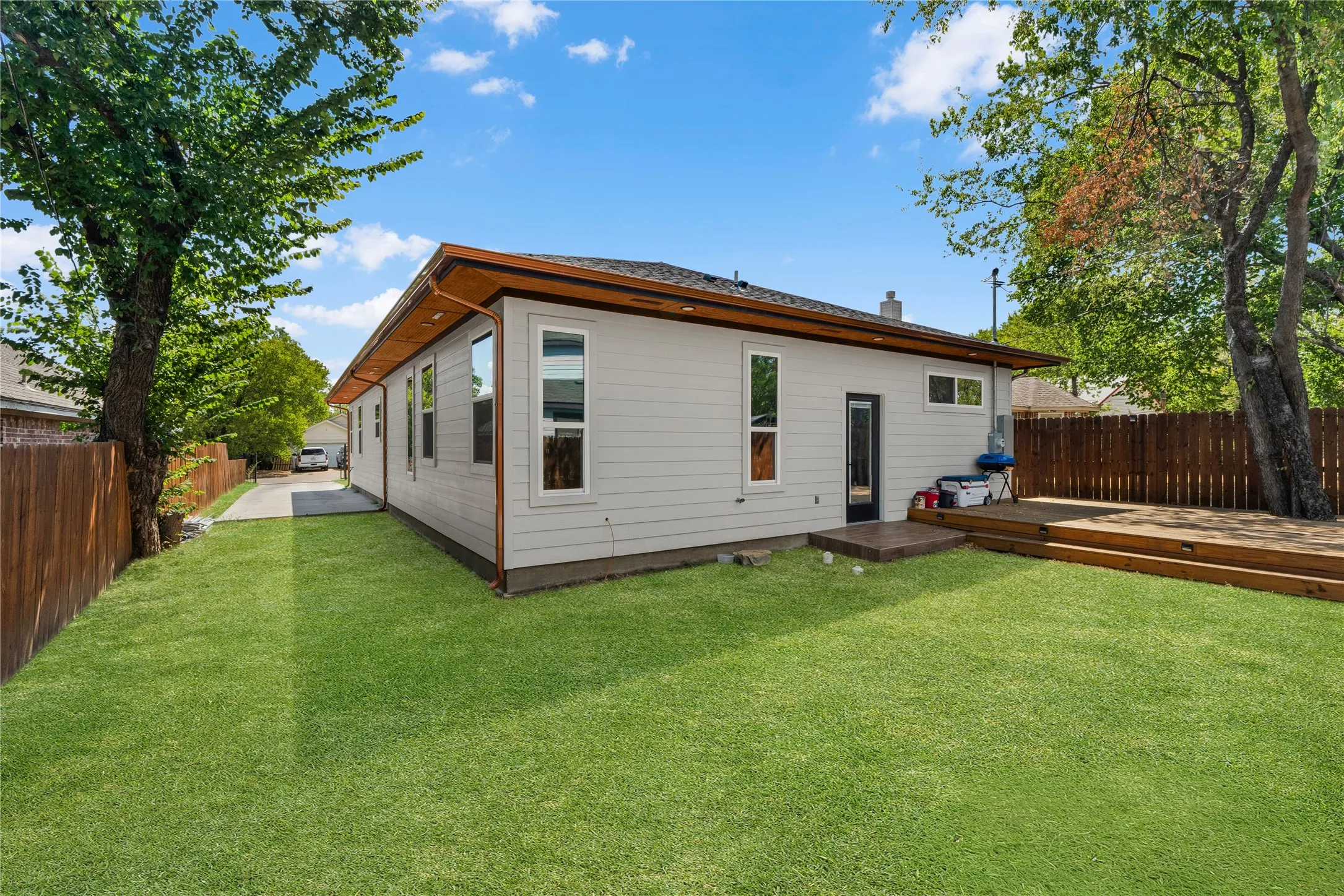 Spacious grassy yard with an expansive wood deck, white vertical siding, and multiple windows