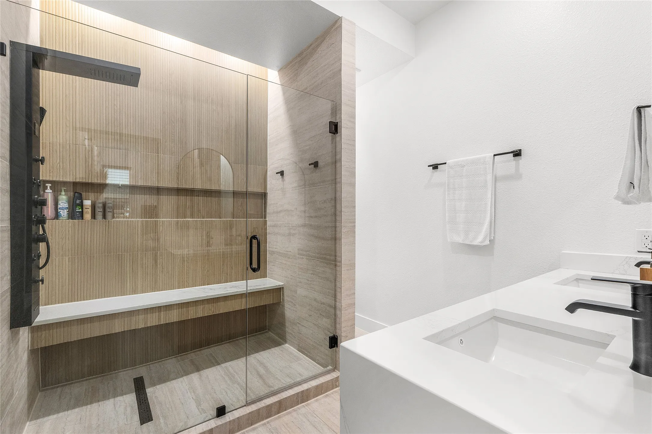Walk-in shower with a built-in bench, integrated shelving, and a dark-finish shower panel