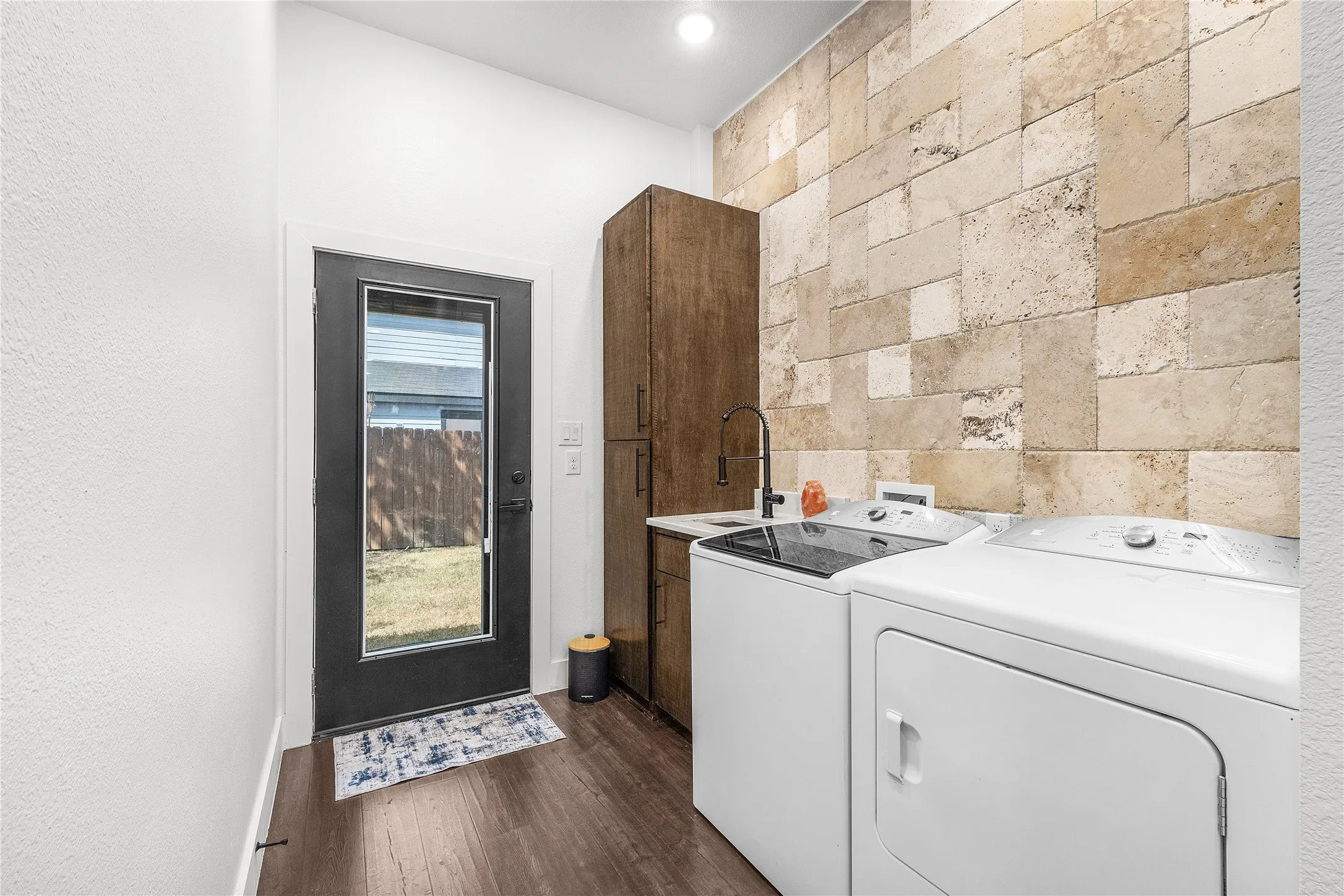 Laundry area featuring wood-finish flooring, a full-lite exterior door, built-in cabinetry, a utility sink with a matte black faucet, and a stone accent wall