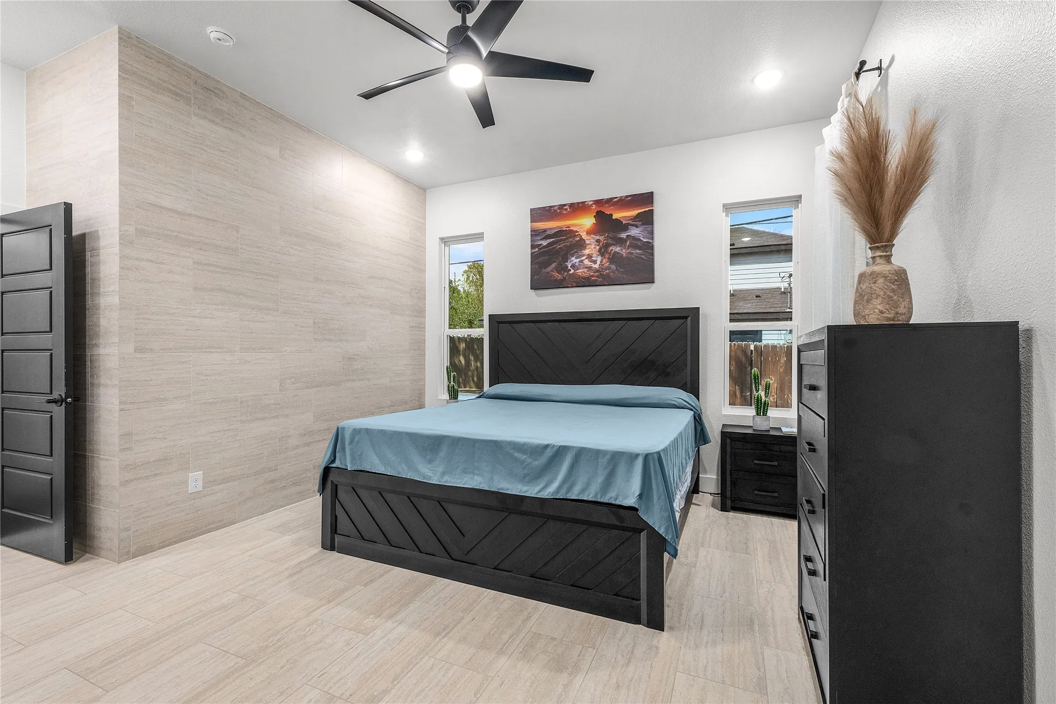 Master bedroom featuring a wood-finish plank floor, black upholstered bed frame, black dresser with multiple drawers, ceiling fan with integrated lighting, and recessed ceiling lights