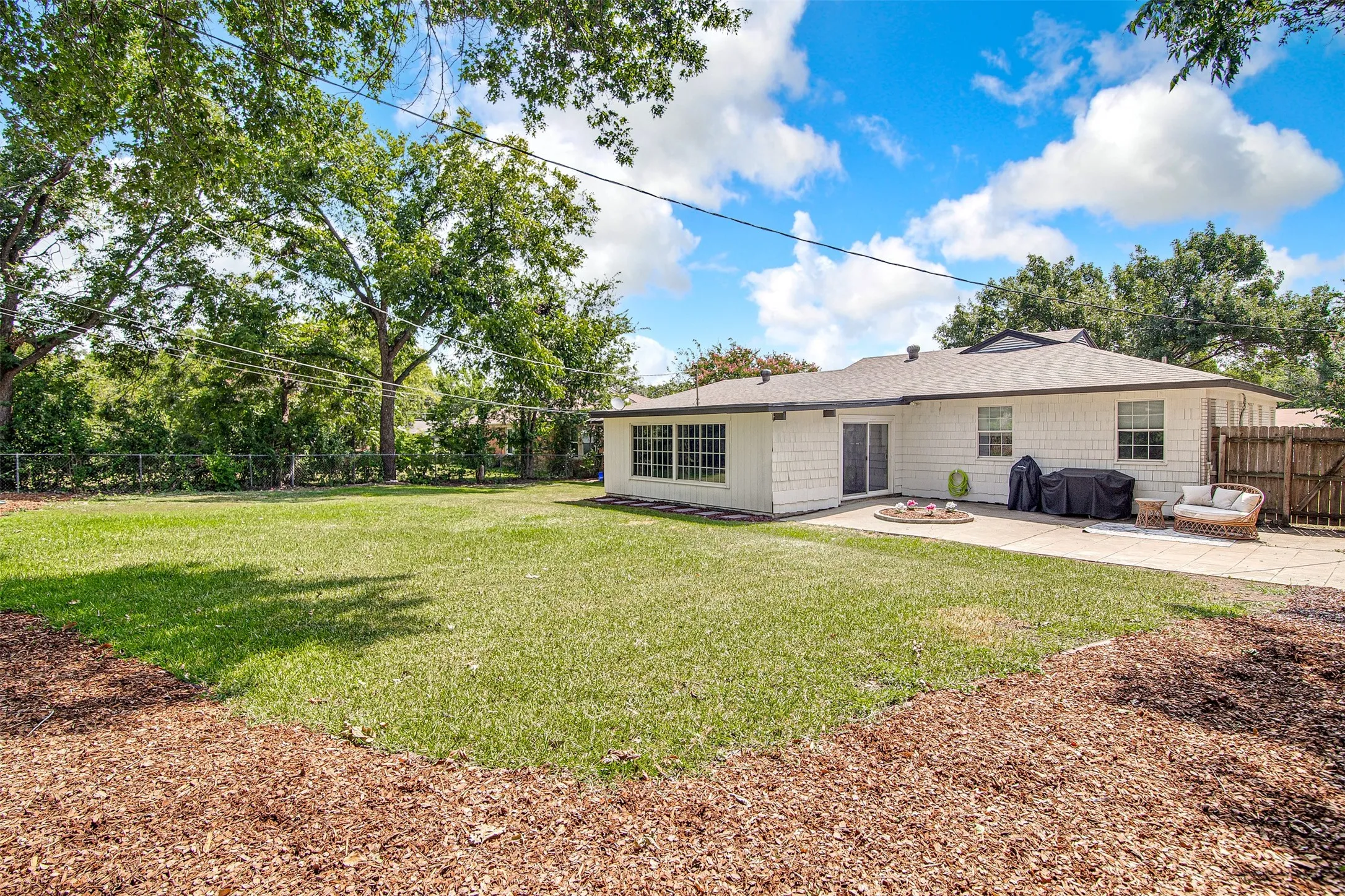 Expansive grassy yard with mature perimeter trees, a rear patio, and white exterior siding
