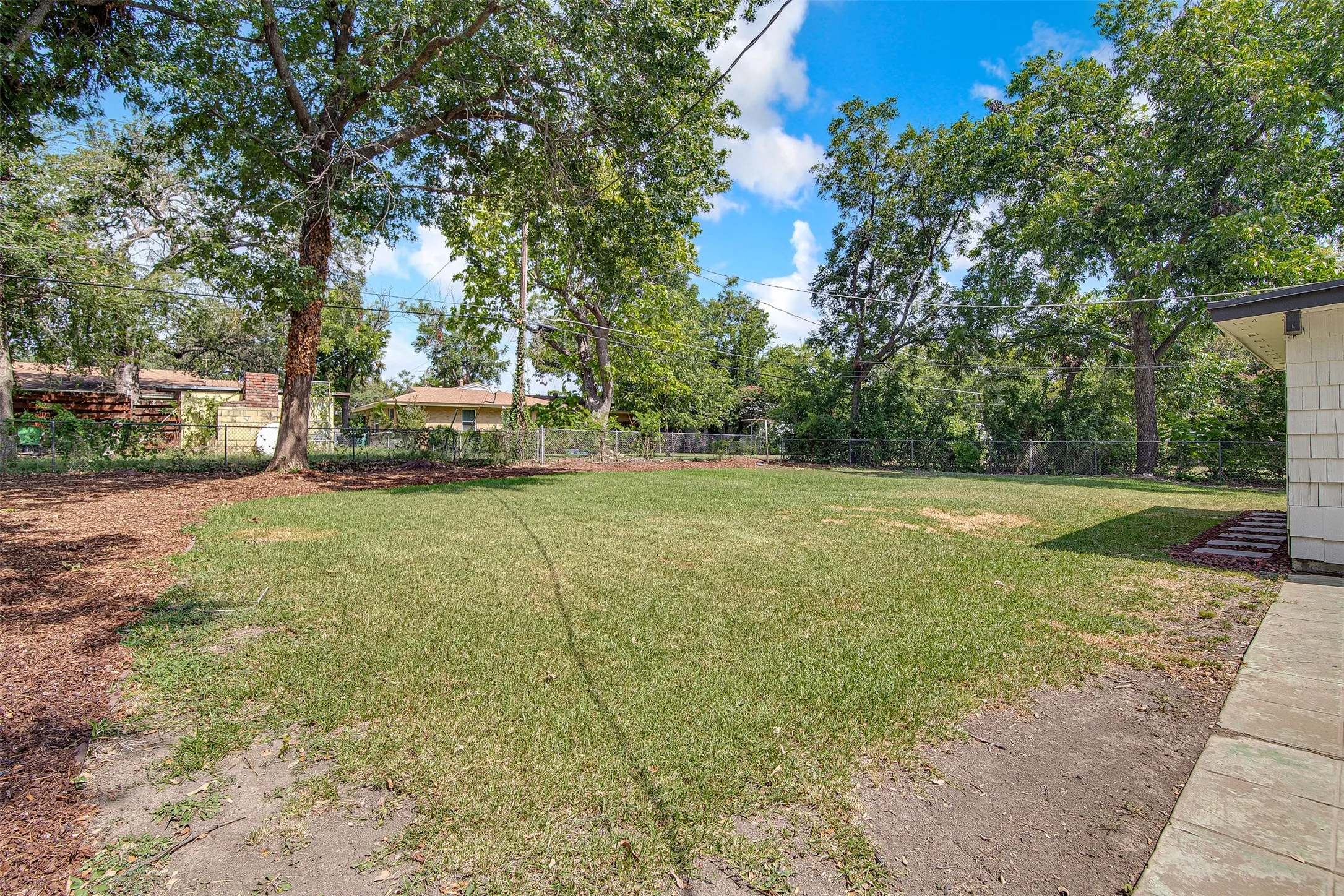 Expansive grassy yard with mature trees and a side concrete patio