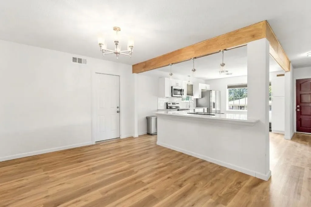 Wood-finish flooring, white paneled door, kitchen pass-through with breakfast bar, stainless steel appliances, and white cabinetry