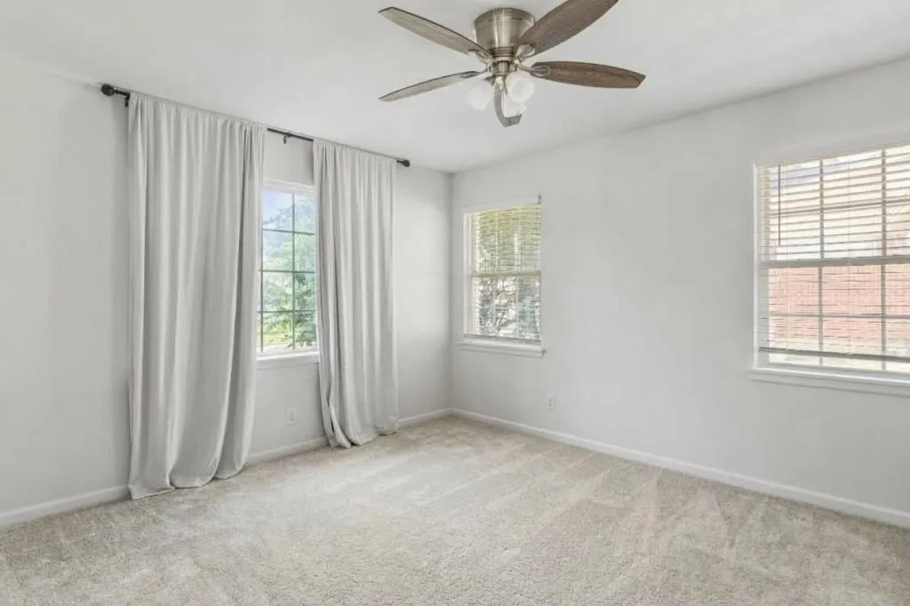 Wall-to-wall carpeting, three windows with blinds, ceiling fan with light fixture, and neutral wall paint
