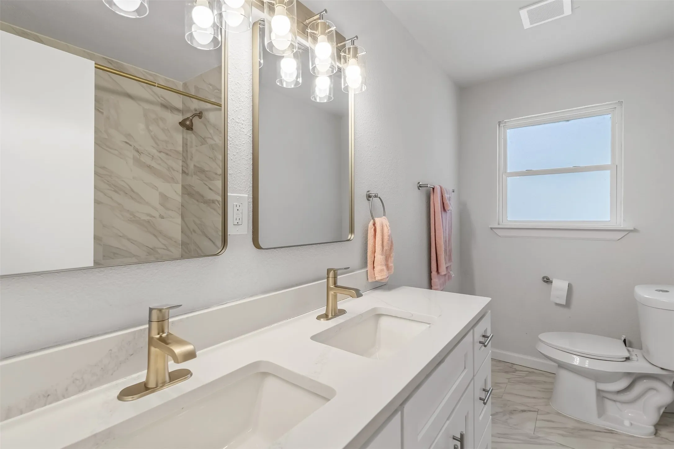 Dual vanity with integrated sinks and brushed gold fixtures, white cabinetry, rectangular framed mirrors, and overhead lighting
