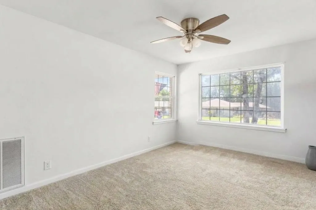 Ceiling fan with light fixture, two windows, wall-to-wall carpeting, and white painted walls