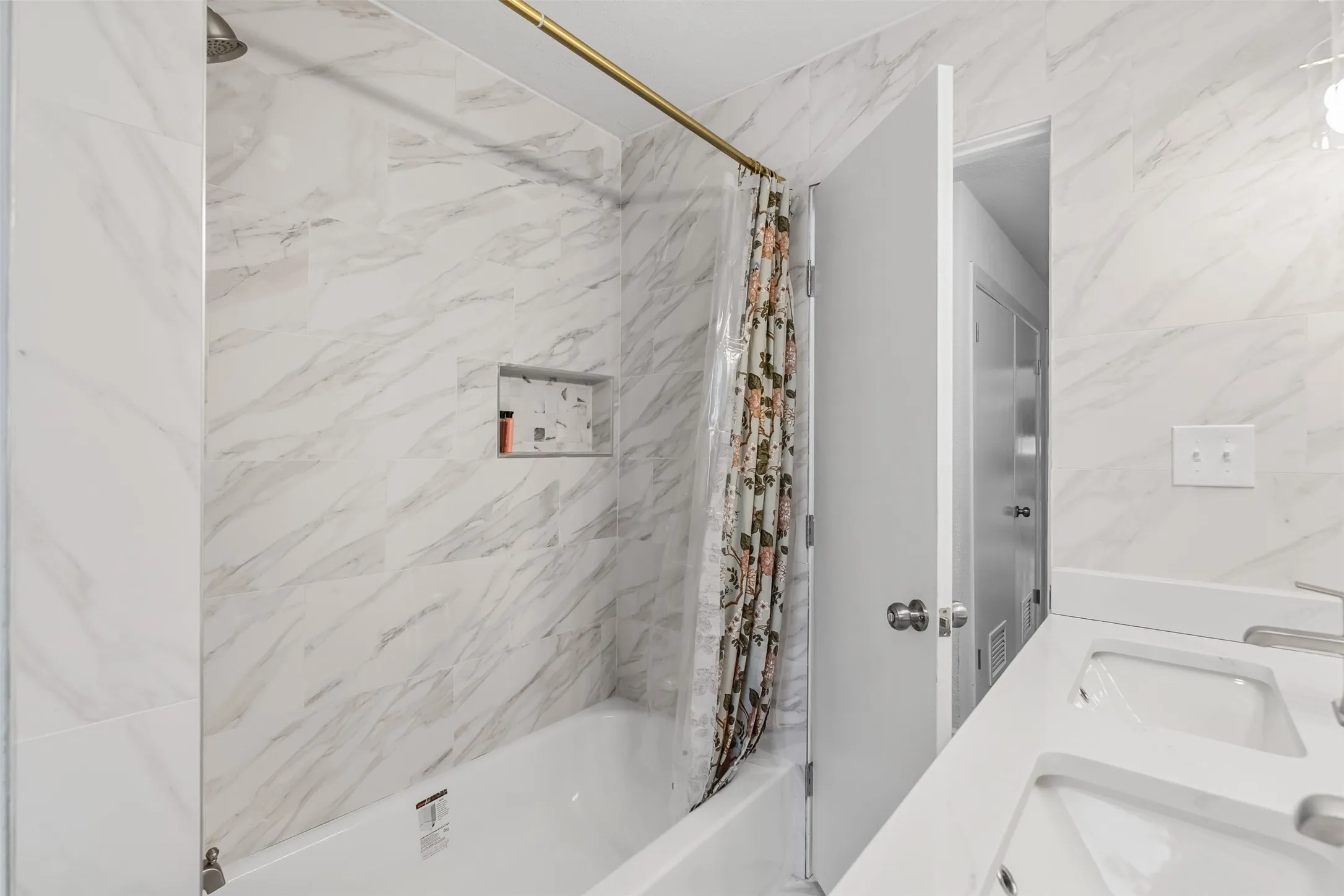 Bathroom featuring a built-in tub with a showerhead, wall-mounted shower niche, double vanity with integrated sinks, and polished chrome faucets