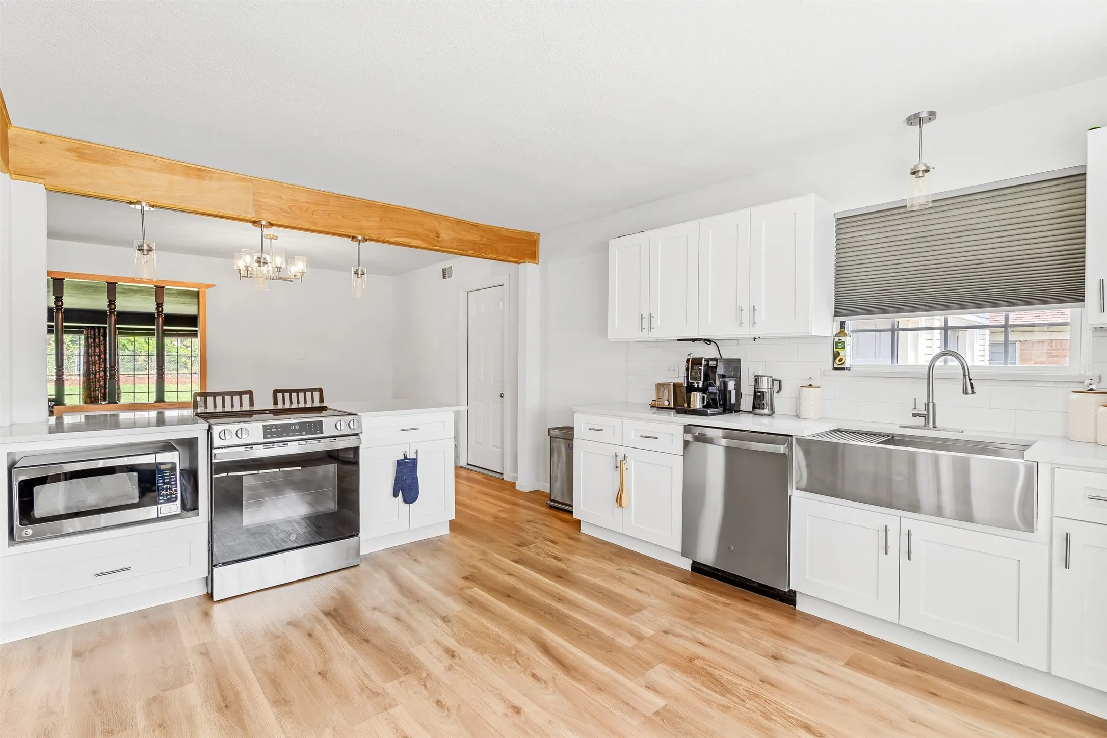 Kitchen featuring wood-finish flooring, white cabinetry, stainless steel appliances, and a farmhouse-style sink