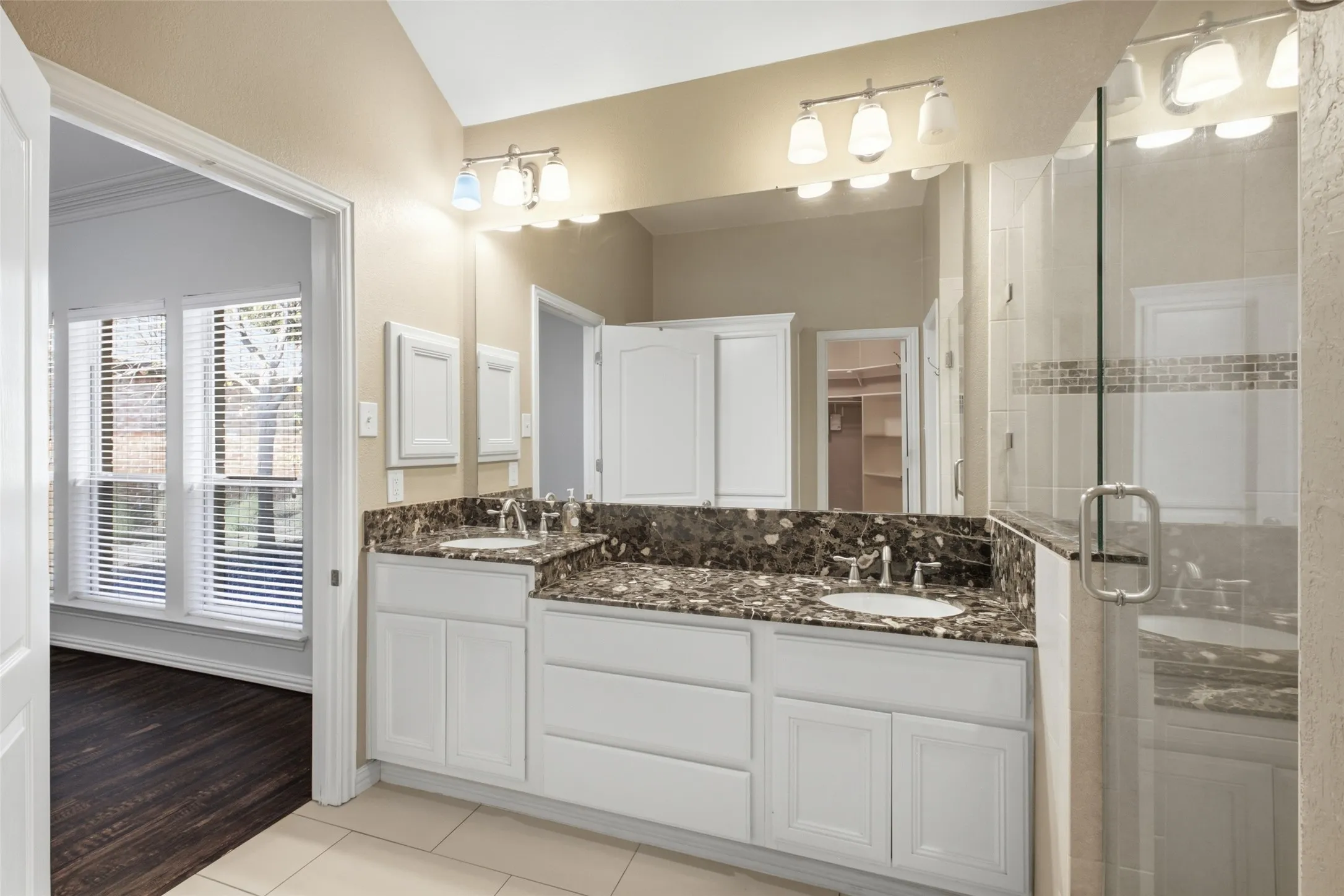 Dual vanity with undermount sinks, stone countertop, white cabinetry, and glass-enclosed shower