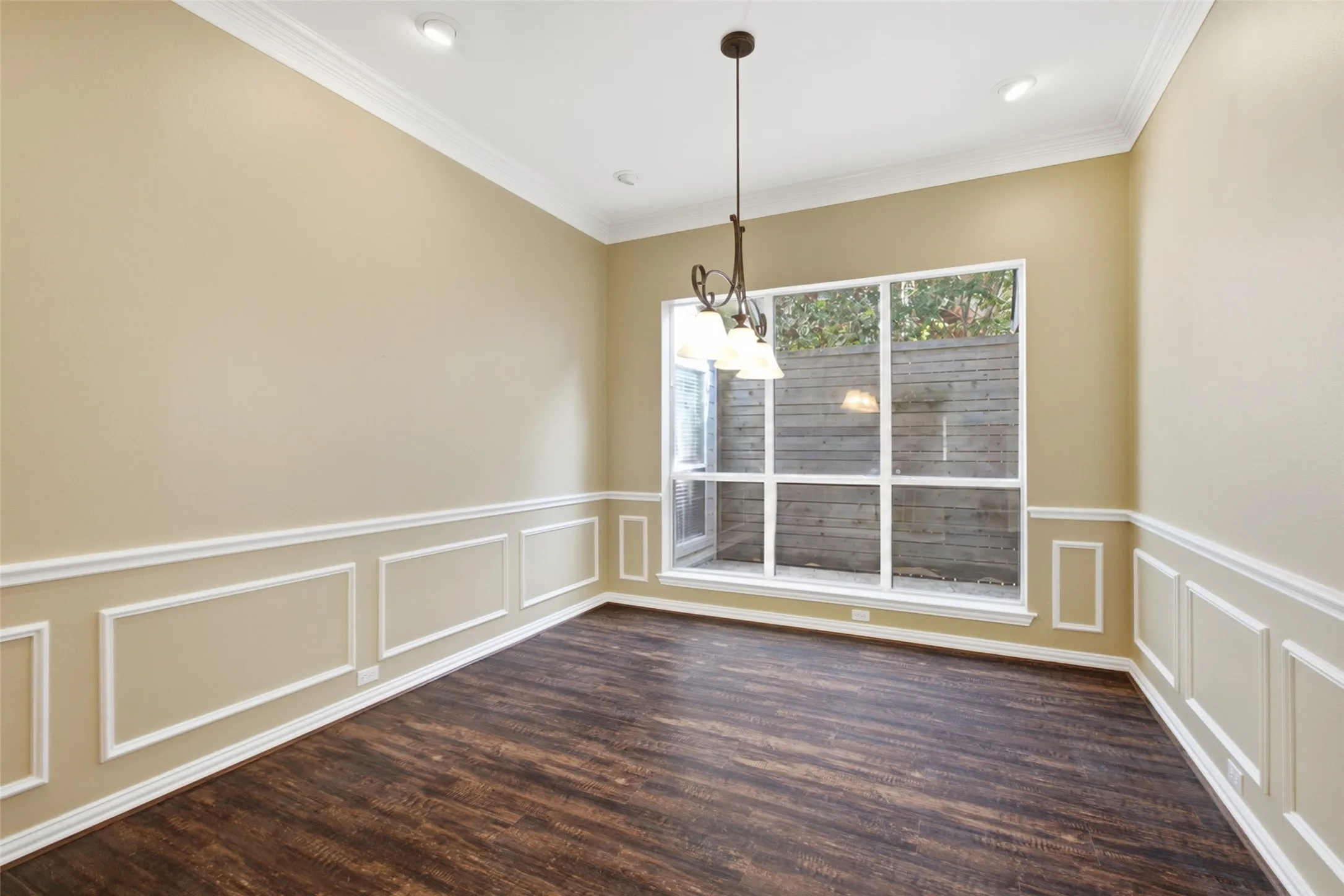 Formal dining in full wainscoting and crown, with a wrought-iron chandelier and garden window