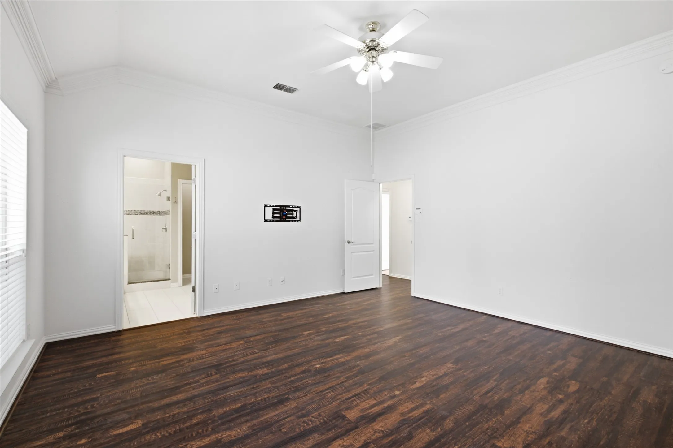 Vaulted ceiling with crown molding, dark wood-finish flooring, ceiling fan with integrated lighting, and an additional room accessible through a doorway