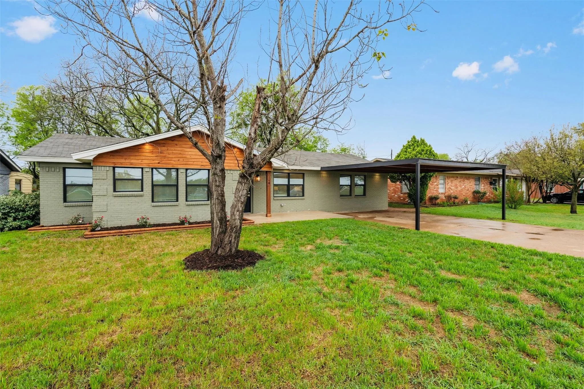 Brick exterior with painted finish, horizontal wood-finish siding, multiple windows with black frames, and a metal carport