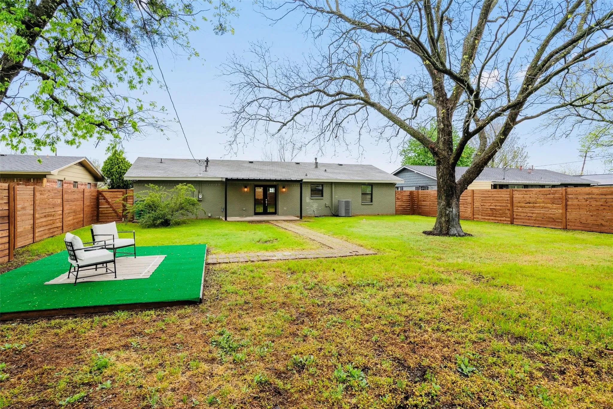 Expansive backyard featuring a manicured lawn, established shade tree, and wood panel fencing