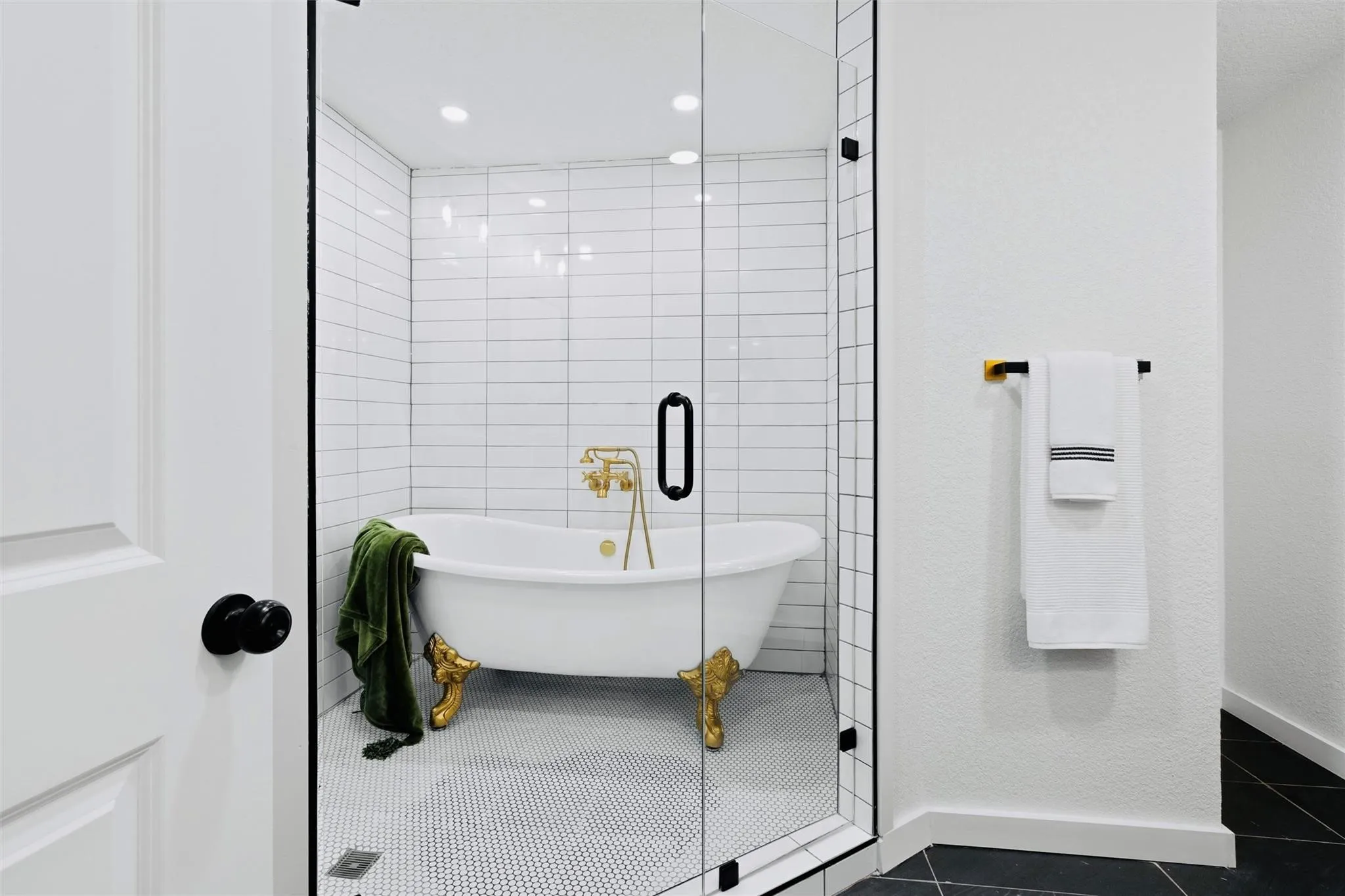 Clawfoot tub with gold-tone hardware, enclosed within a glass shower with white subway tile