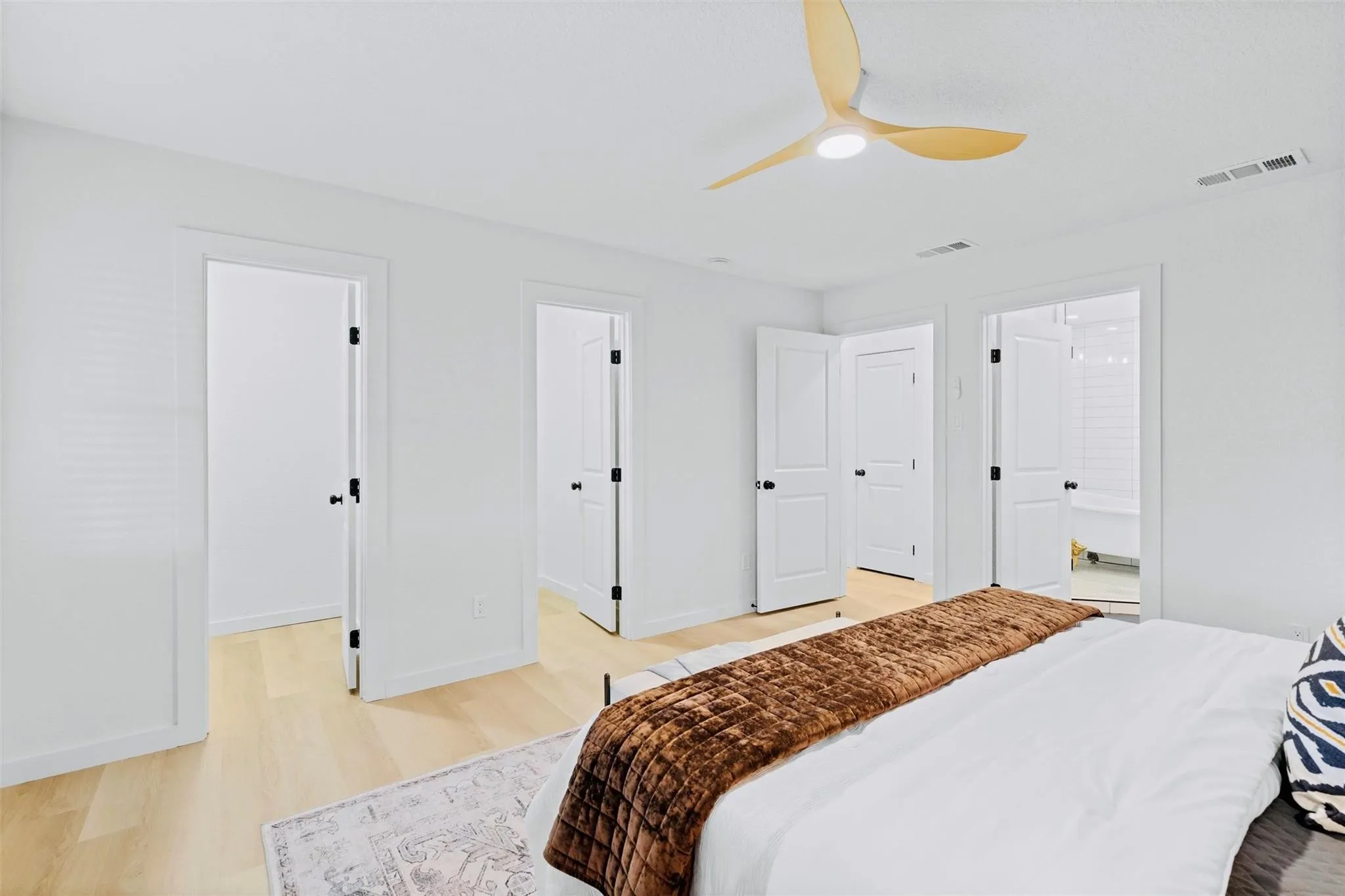 Light wood-finish flooring, white doors with matte black hardware, and a modern ceiling fan with wood-finish blades