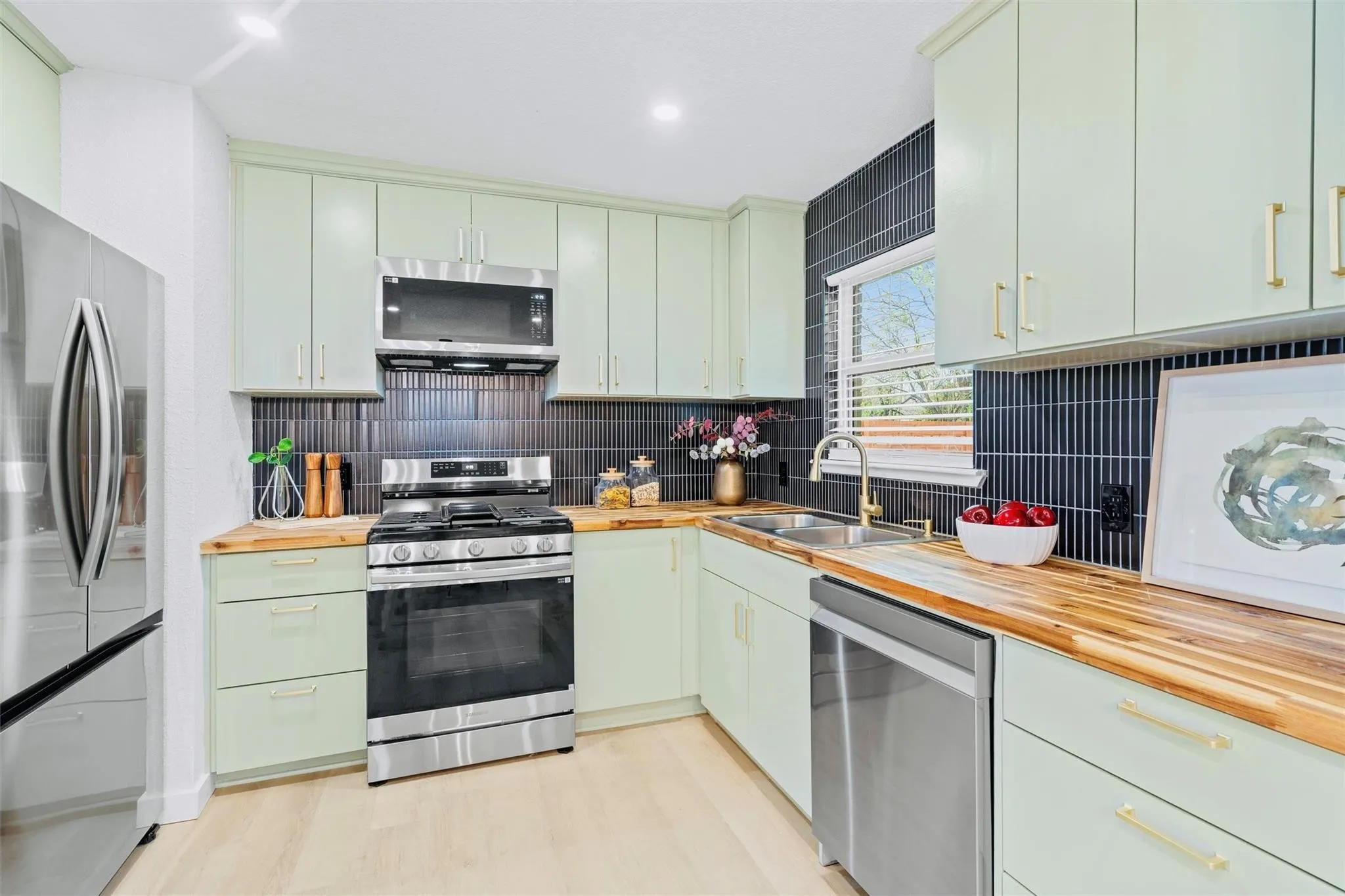 Kitchen featuring light green cabinetry, wood-finish countertops, stainless steel appliances, and a dark vertical tile backsplash