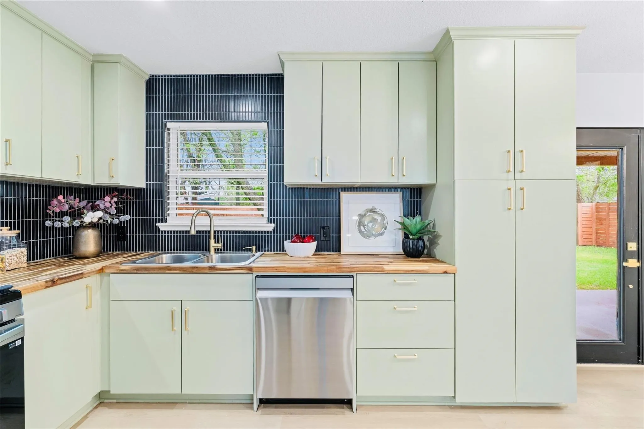 Kitchen featuring light-toned cabinetry, wood-finish countertops, stainless steel appliances, a dual basin sink with a gooseneck faucet, and a dark tile backsplash