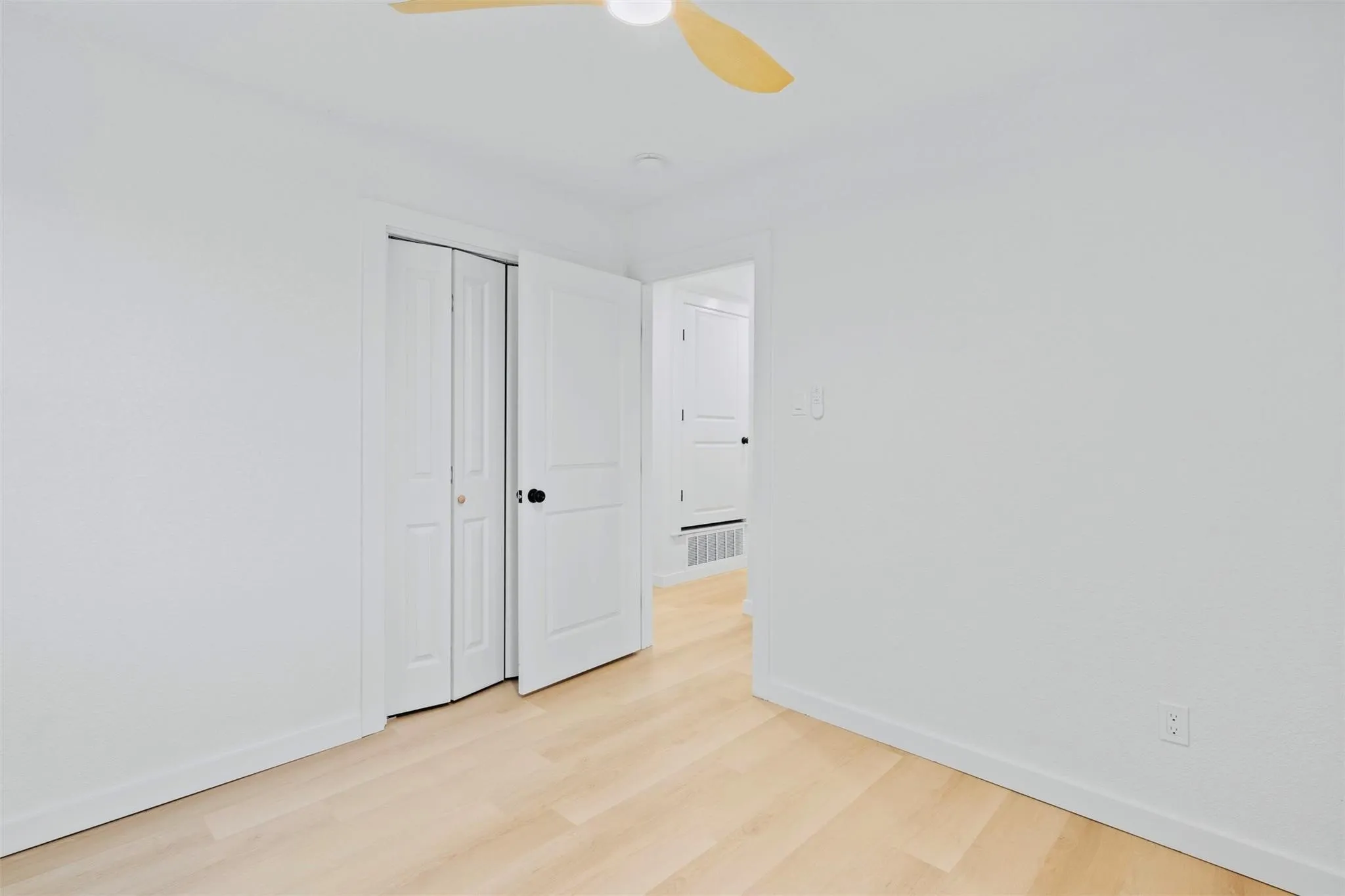 Smooth white walls, wood-finish flooring, white bi-fold closet doors, white interior door, and a ceiling fan