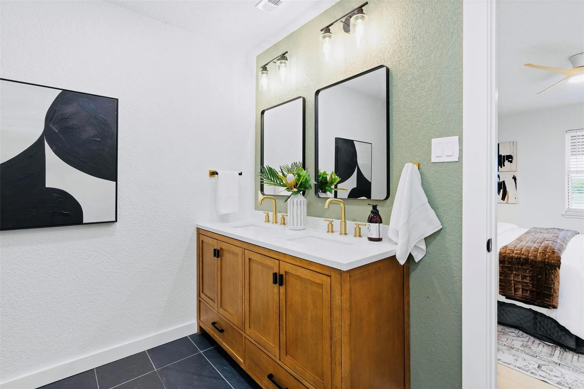 Dual vanity with wood-finish cabinetry, white countertop, and gold-finish fixtures