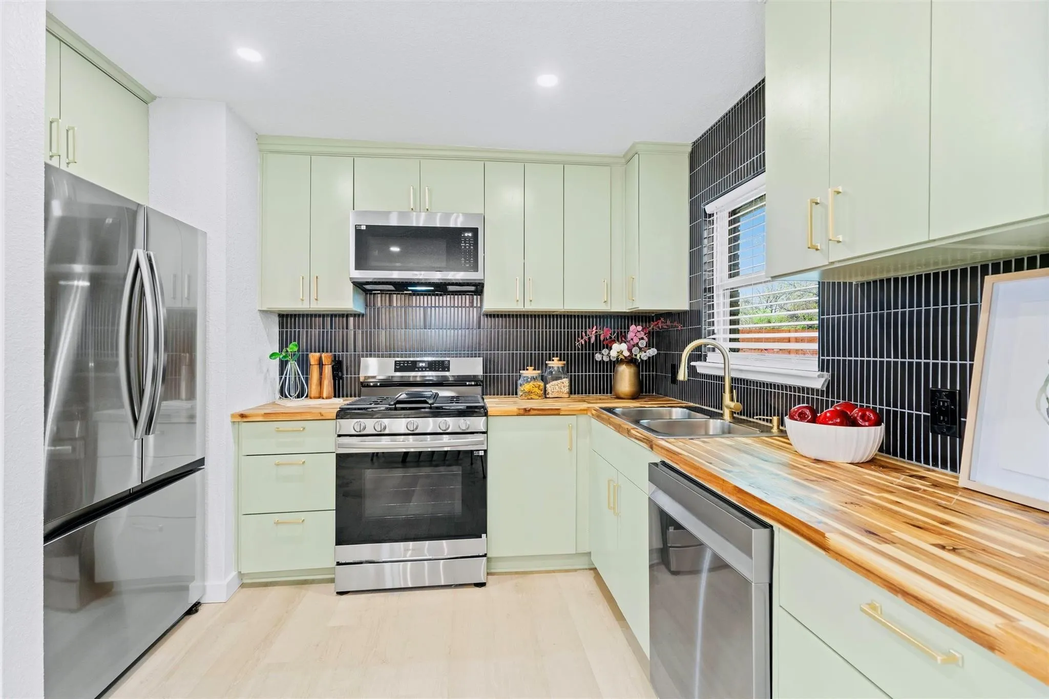 Kitchen featuring stainless steel appliances, light green cabinetry, wood-finish countertops, black subway tile backsplash, and light wood-finish flooring