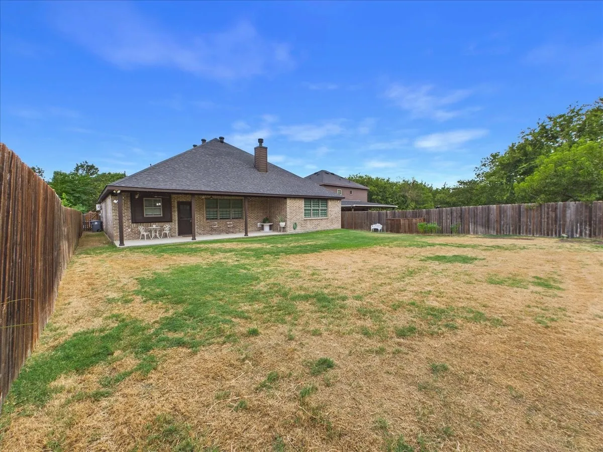 Expansive backyard featuring a full perimeter wood fence, a large covered patio, and a brick exterior