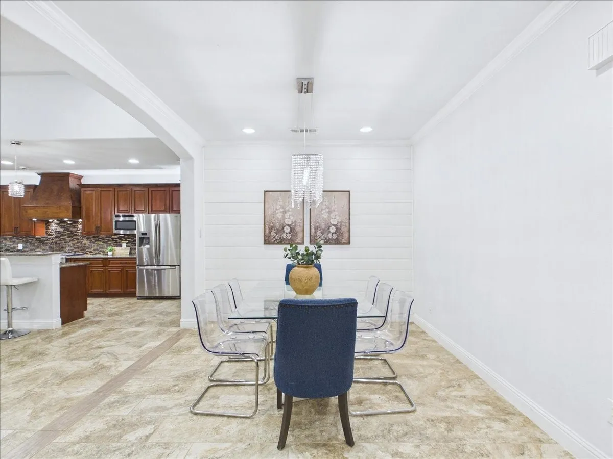 Open concept living space featuring neutral-toned tile flooring, white walls, crown molding, and a modern chandelier