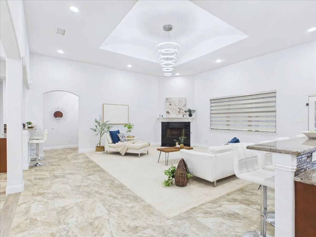 Recessed lighting, tray ceiling with contemporary chandelier, tiled flooring, built-in fireplace, and a kitchen pass-through with bar seating