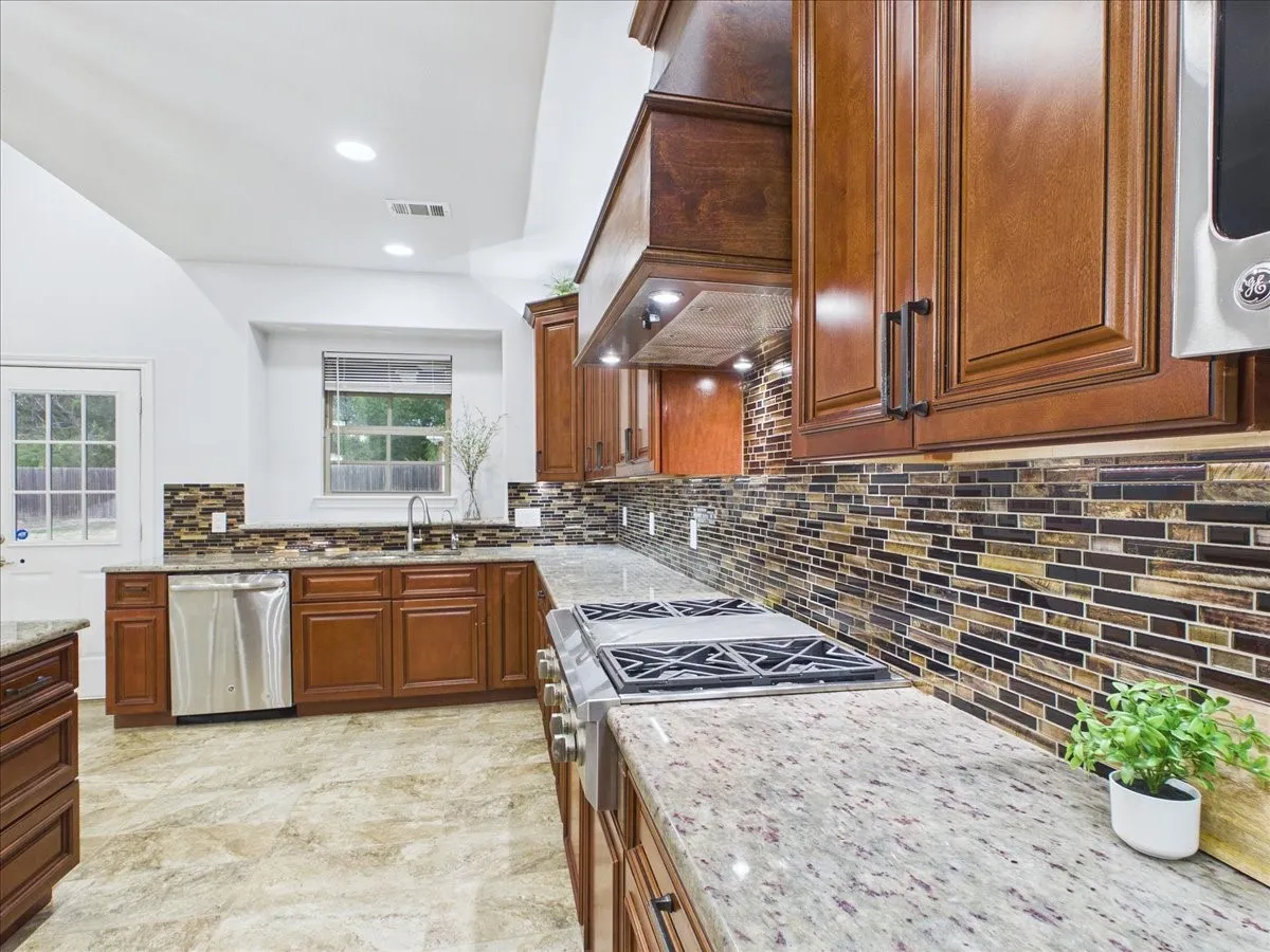 Kitchen featuring wood-finish cabinetry, light-colored granite countertops, and a full-height mosaic tile backsplash