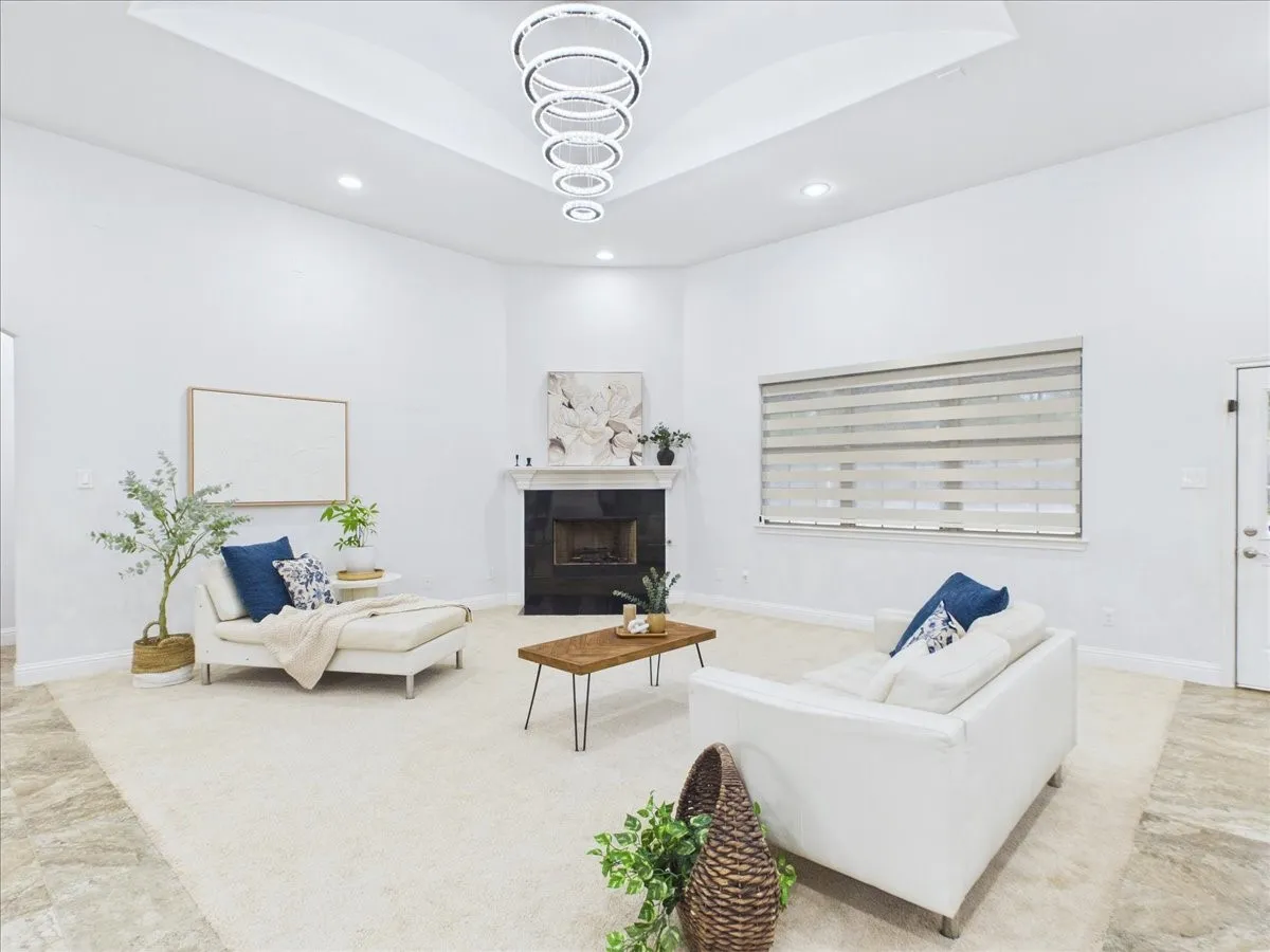 Recessed lighting, contemporary chandelier, tray ceiling, fireplace with dark surround, and large window with blinds