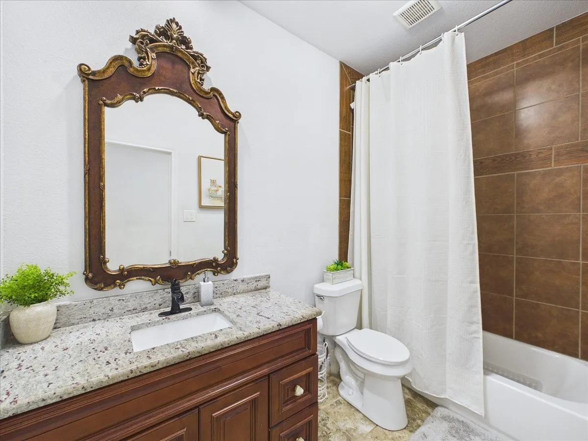 Bathroom featuring a wood vanity with granite countertop, integrated sink, and dark bronze faucet