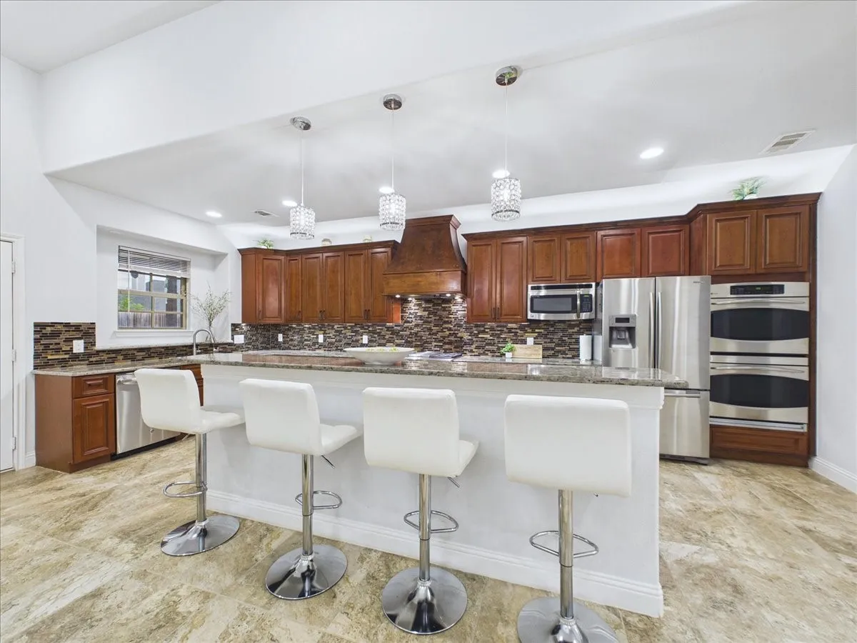 Stainless steel appliances, recessed lighting, wood cabinetry, tile flooring, and a stone backsplash