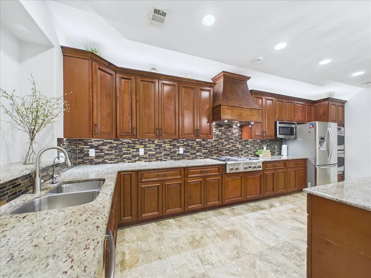 Kitchen featuring wood cabinetry, light-toned stone countertops, and a mosaic tile backsplash