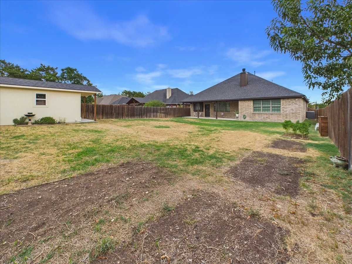 Expansive backyard featuring a detached structure, privacy fencing, and a brick exterior residence with a covered patio