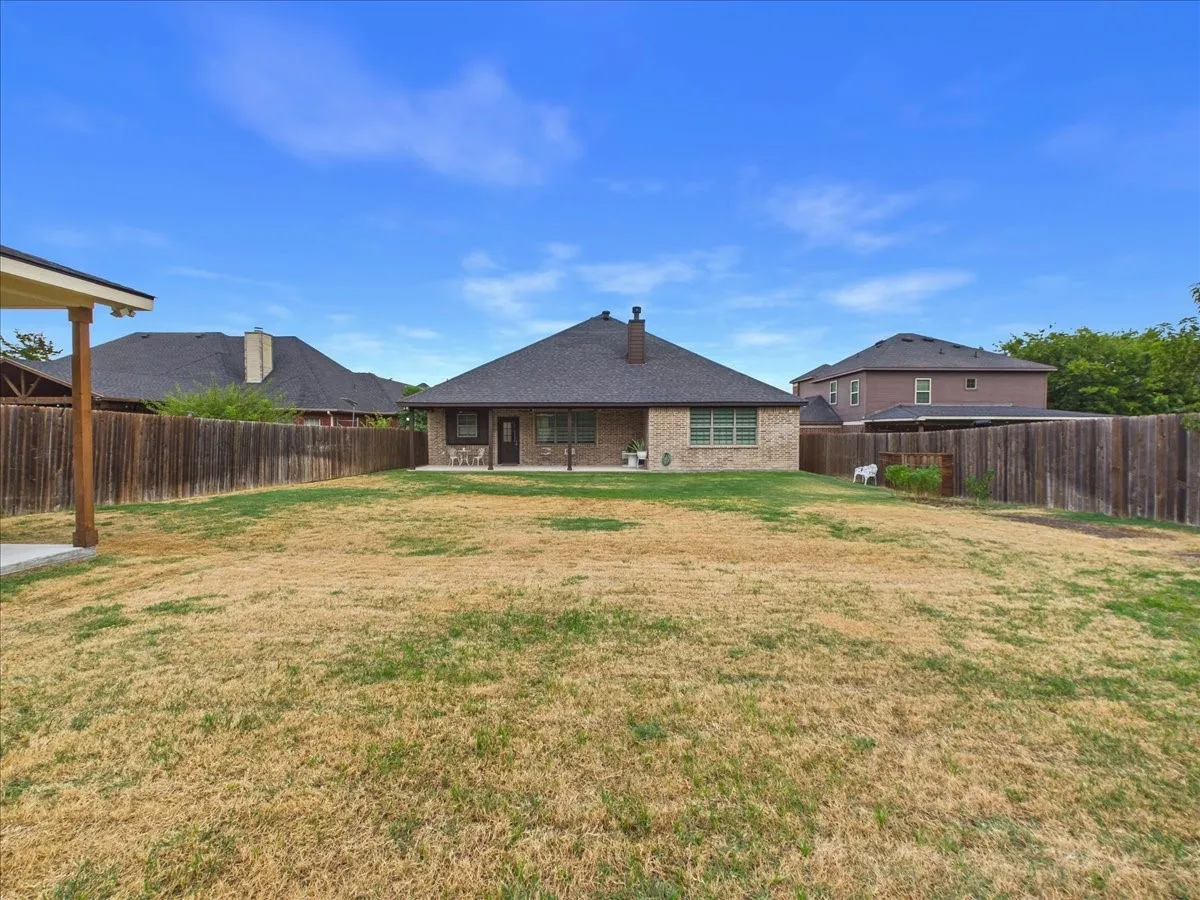 Expansive backyard with a wood privacy fence, a covered patio, and a brick exterior