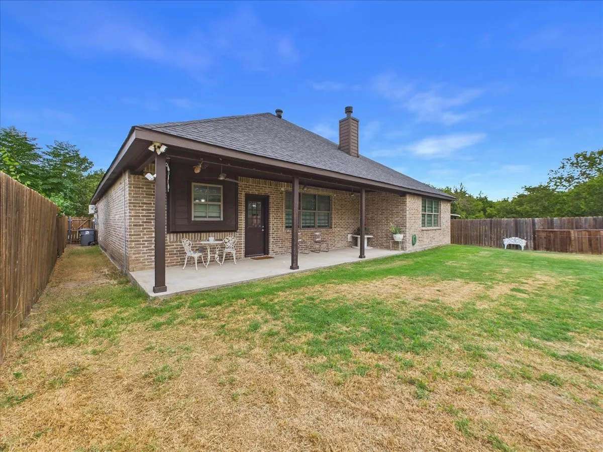 Brick exterior featuring a covered patio, a wood privacy fence, and a chimney