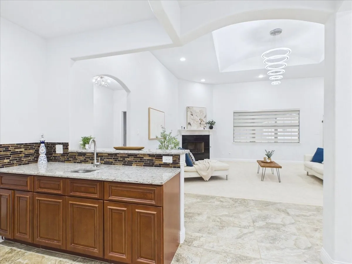 Custom wet bar with integrated sink and granite-style countertop, tile backsplash, wood-finish cabinetry, and recessed lighting