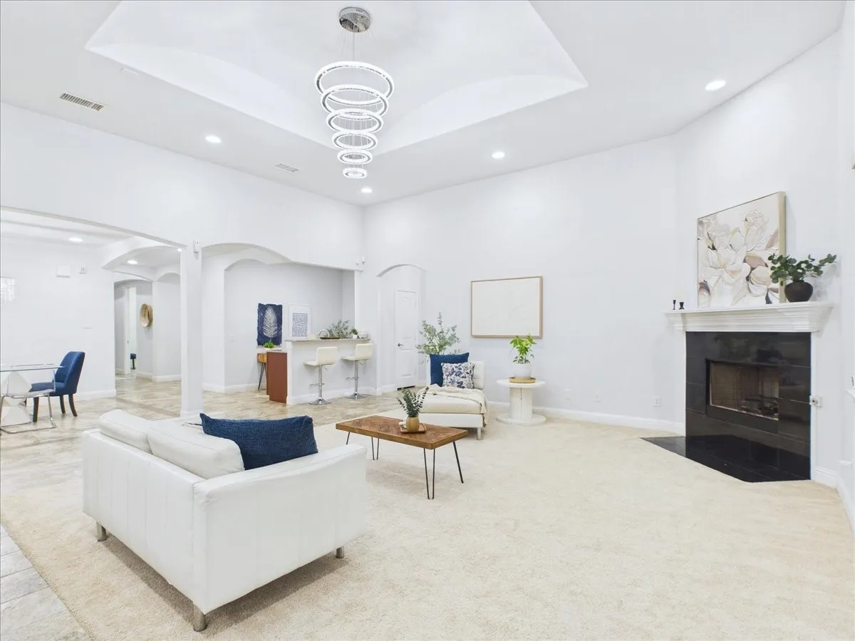 Recessed lighting, tray ceiling with a contemporary chandelier, built-in fireplace with a dark surround, and arched doorways