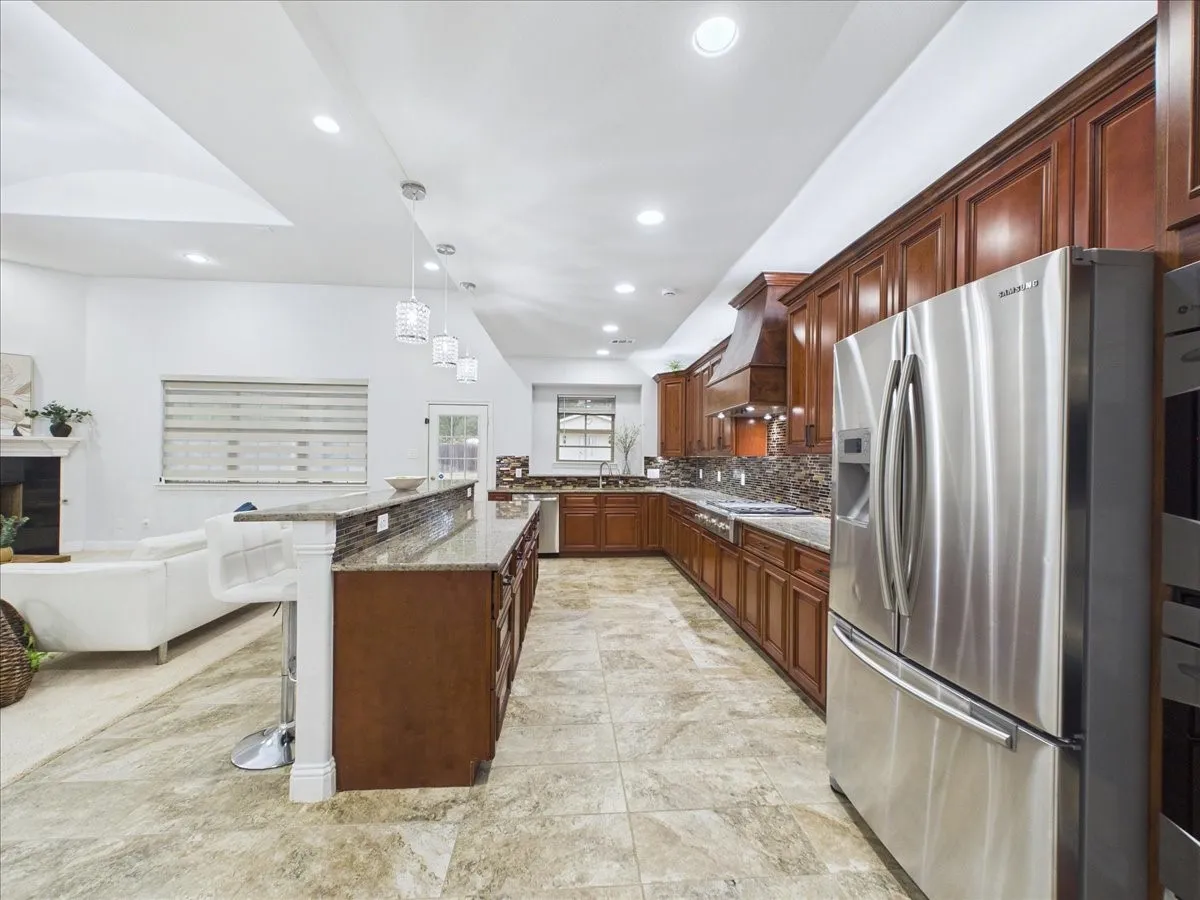 Kitchen featuring stainless steel appliances, wood cabinetry, stone countertops, and tile flooring